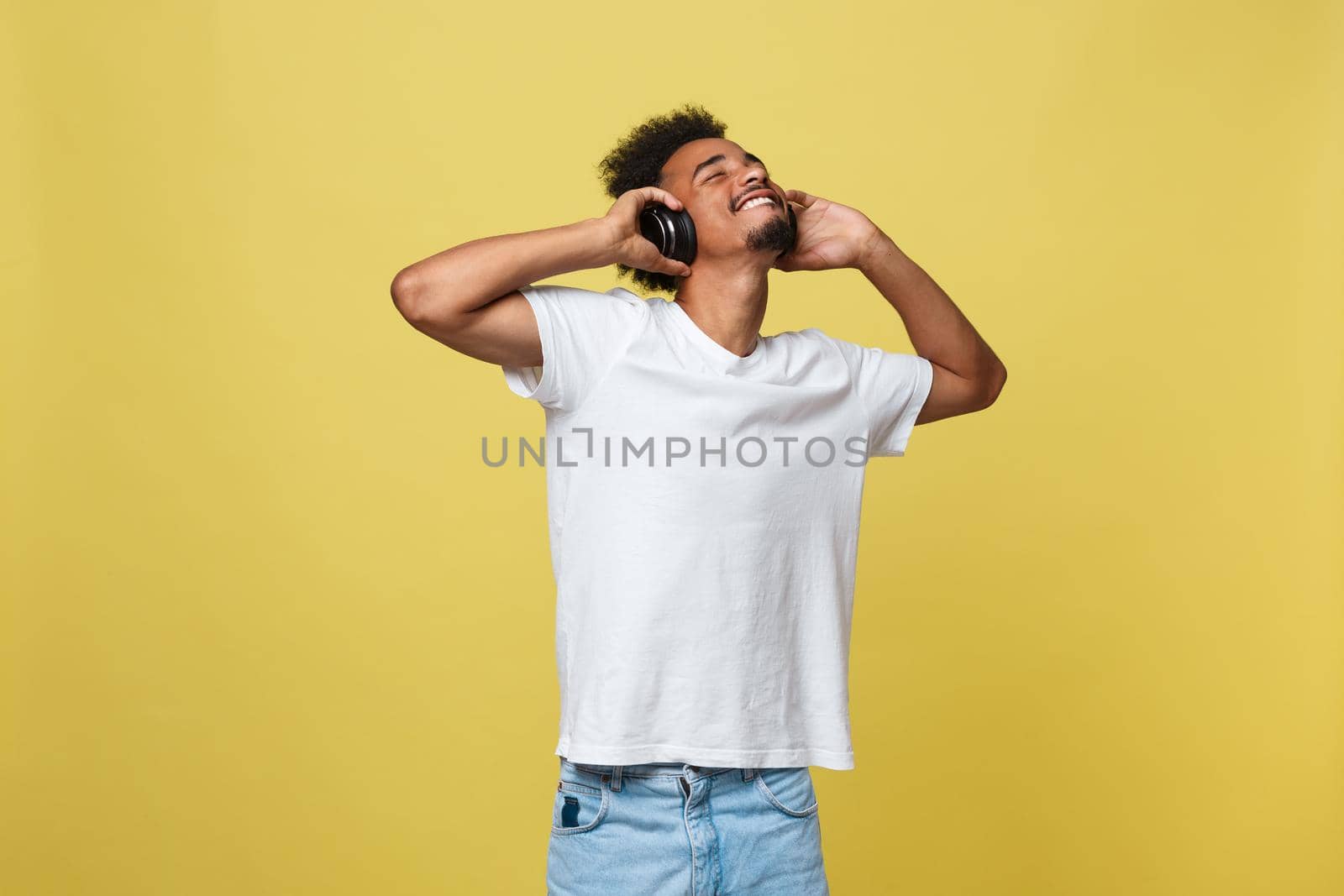 Young African American man wearing headphone and enjoy music over yellow gold Background.