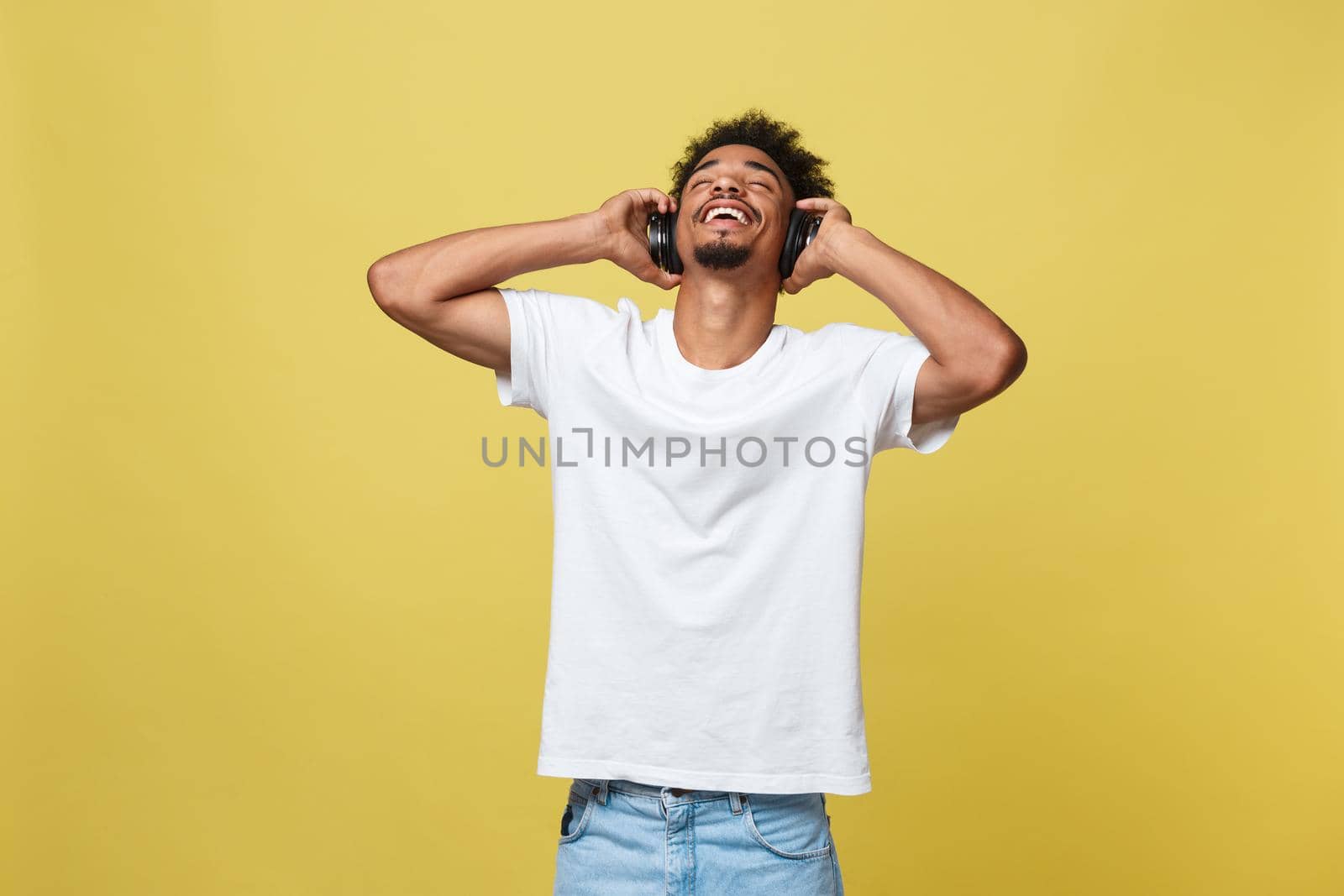 Young African American man wearing headphone and enjoy music over yellow gold Background.