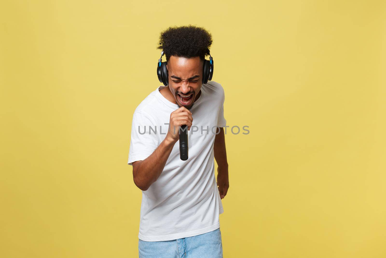 Attractive young dark-skinned man with afro haircut in white t shirt, gesticulating with hands and microphone, dancing and singing on party, having fun. by Benzoix