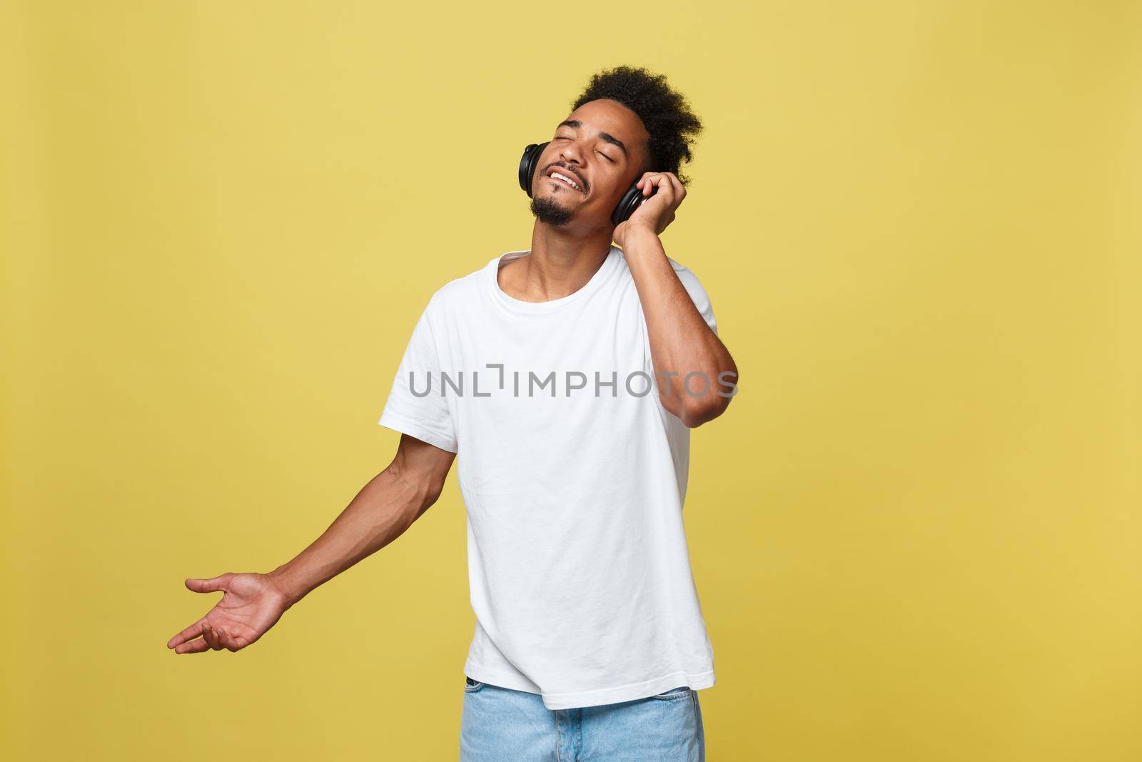 Young black man listening to music over his headphones. Isolated over yellow background. by Benzoix