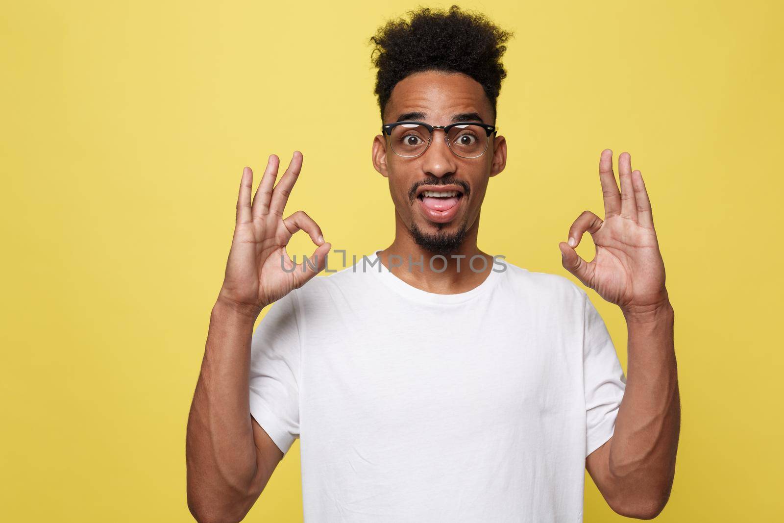 Portrait of happy african-american man showing ok sign and smiling, over yellow background by Benzoix