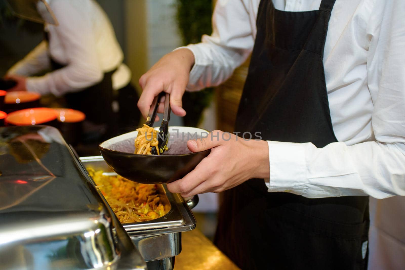 Black bowl with noodles served at a party by a waiter with a black kitchen apron