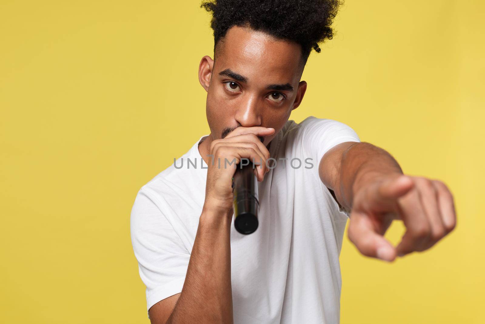 Stylish afro american man singing into microphone isolated on a yellow gold background.