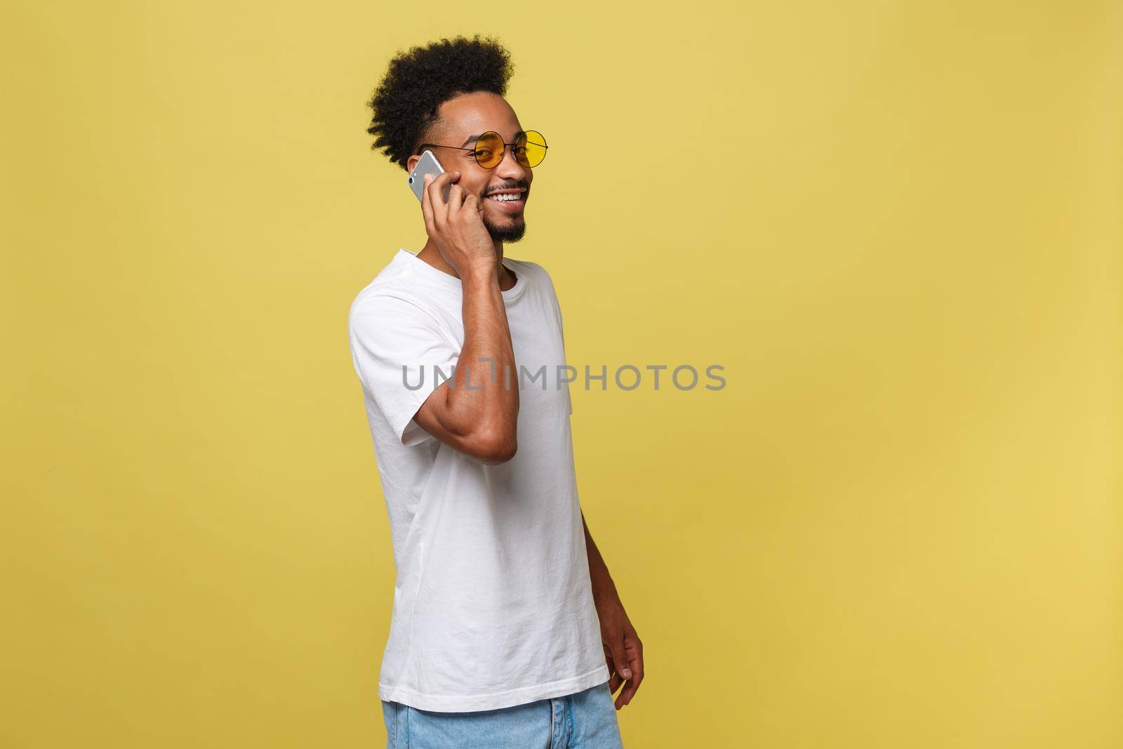 Portrait of cool young black guy talking on cellphone. Isolated on yellow background.