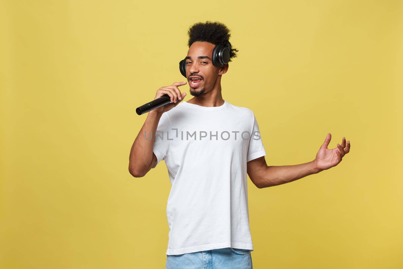 Attractive young dark-skinned man with afro haircut in white t shirt, gesticulating with hands and microphone, dancing and singing on party, having fun. by Benzoix