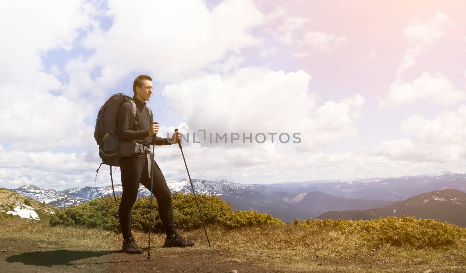 A young man, while hiking in the mountains in winter, looks ahead and admires the stunning mountain landscape. A hiker with tourist equipment climbs to the top of a mountain in a national park.