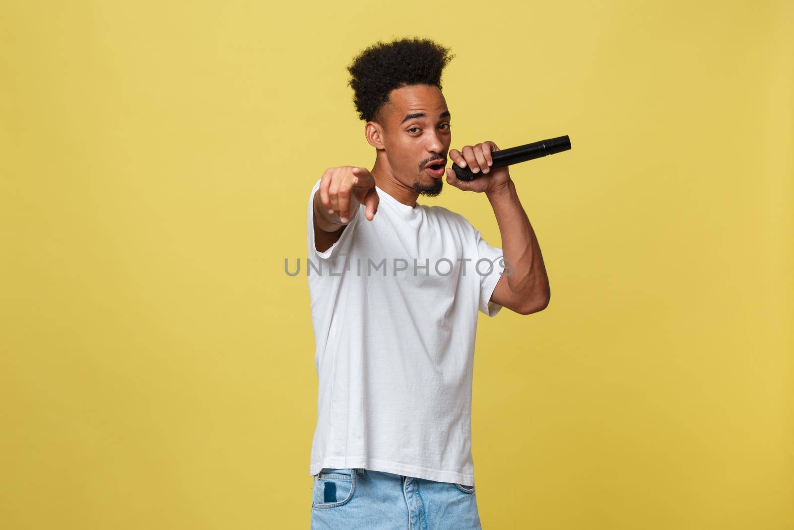 Attractive young dark-skinned man with afro haircut in white t shirt, gesticulating with hands and microphone, dancing and singing on party, having fun. by Benzoix