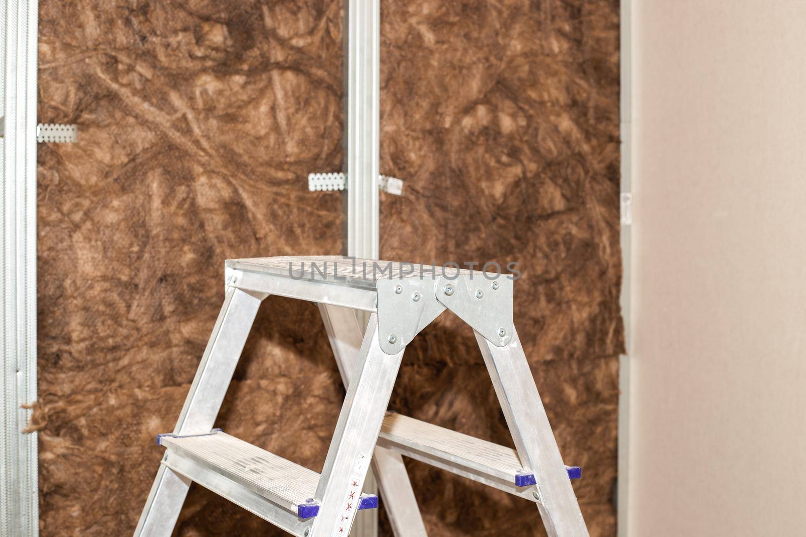 Home repairs. A folding ladder stands against the background of a wall lined with mineral wool for further cladding with plasterboard. Heat insulation and sound insulation of housing.