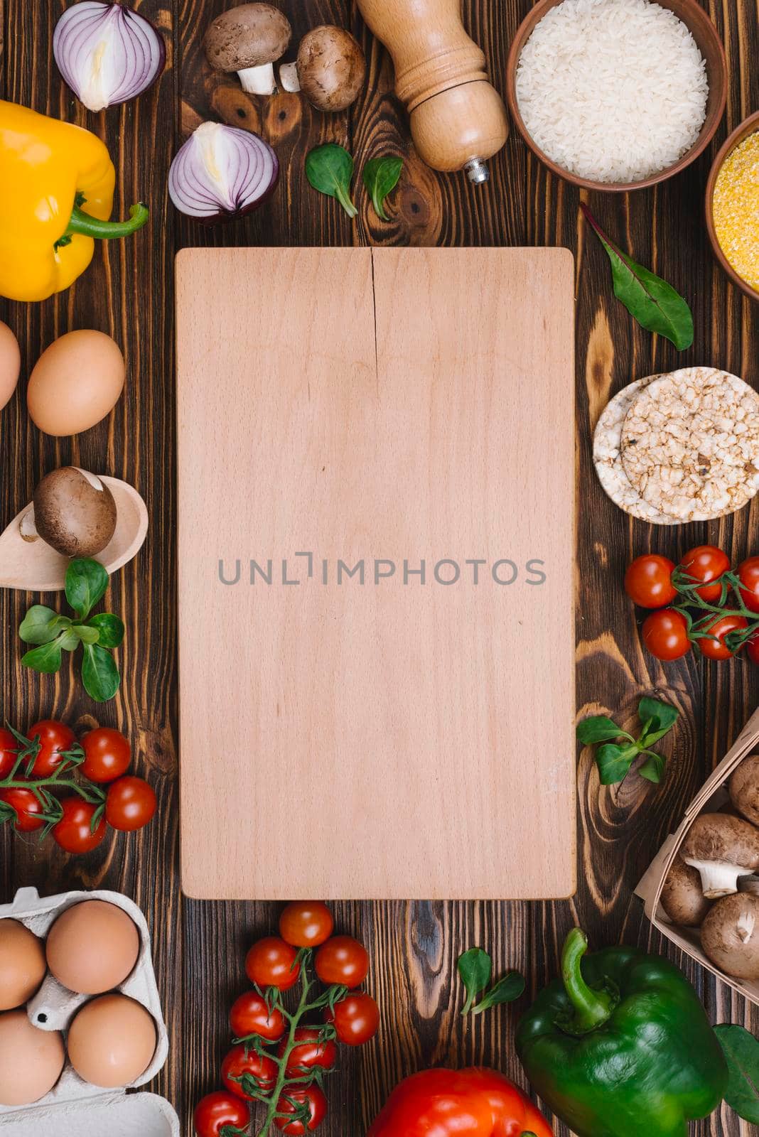 chopping board surrounded with vegetables eggs rice grains desk. High resolution photo