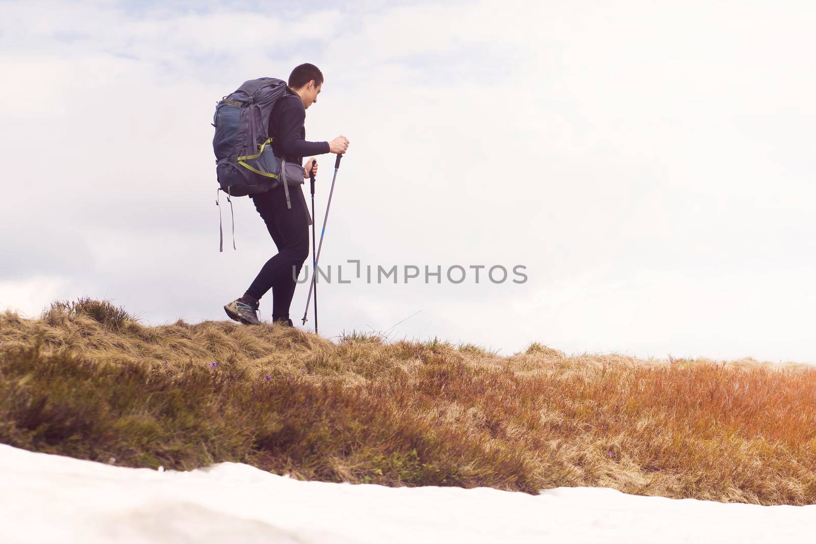 A traveler walks along a trail in the mountains, hiking in the wild in winter alone, with a backpack, camping equipment and trekking poles. The young man enjoys an active lifestyle.