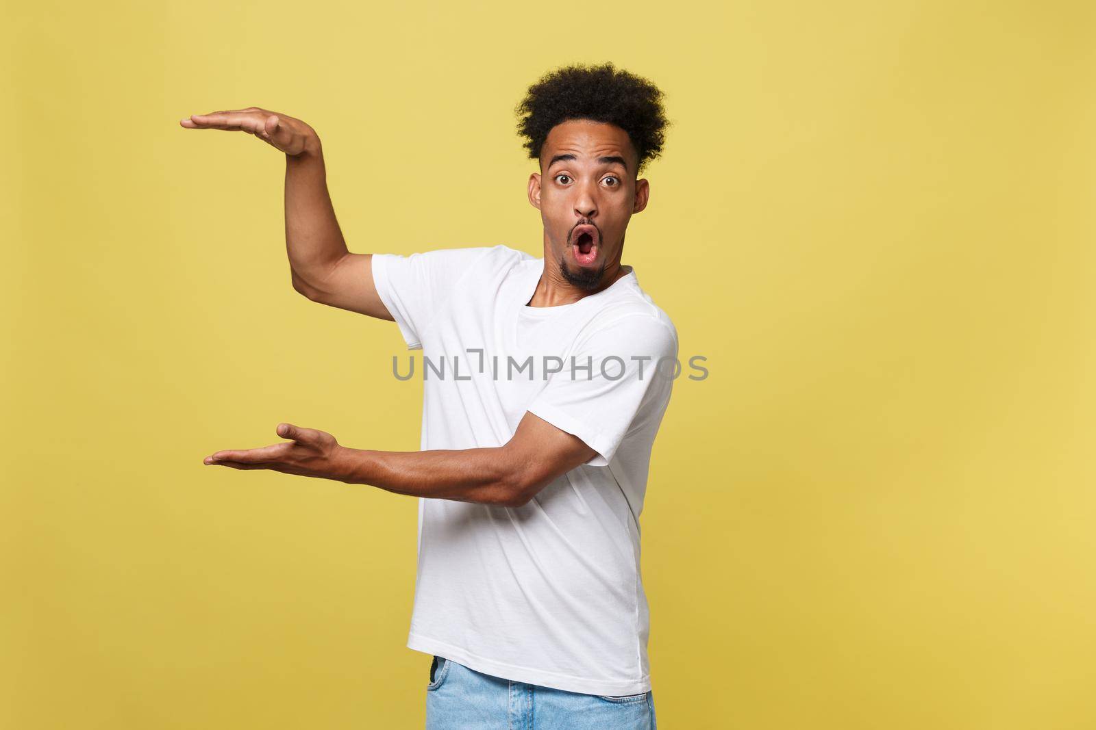 Advertising concept. Portrait of handsome African entrepreneur or office worker wearing suit pointing his finger at yellow studio wall with copy space for your content, looking shocked and surprised