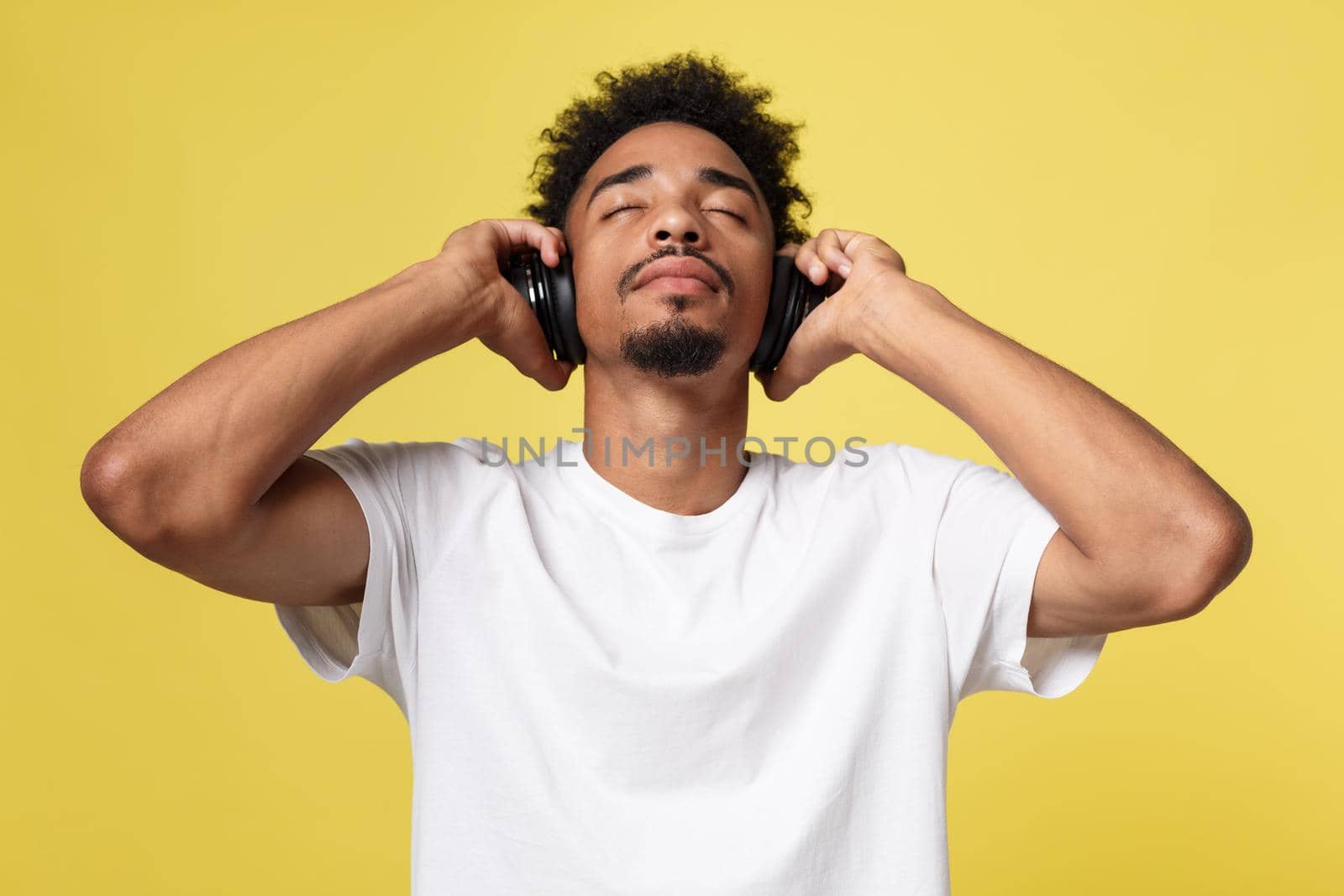 Young African American man wearing headphone and enjoy music over yellow gold Background.