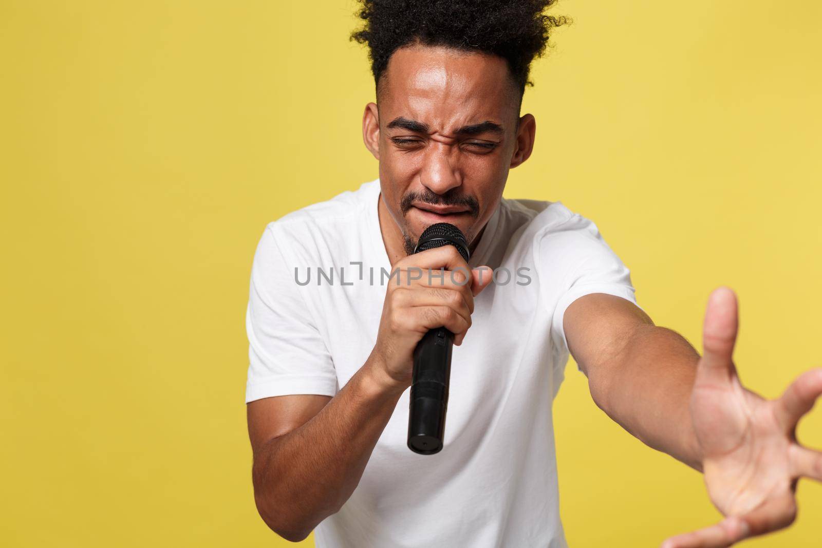 Stylish afro american man singing into microphone isolated on a yellow gold background.