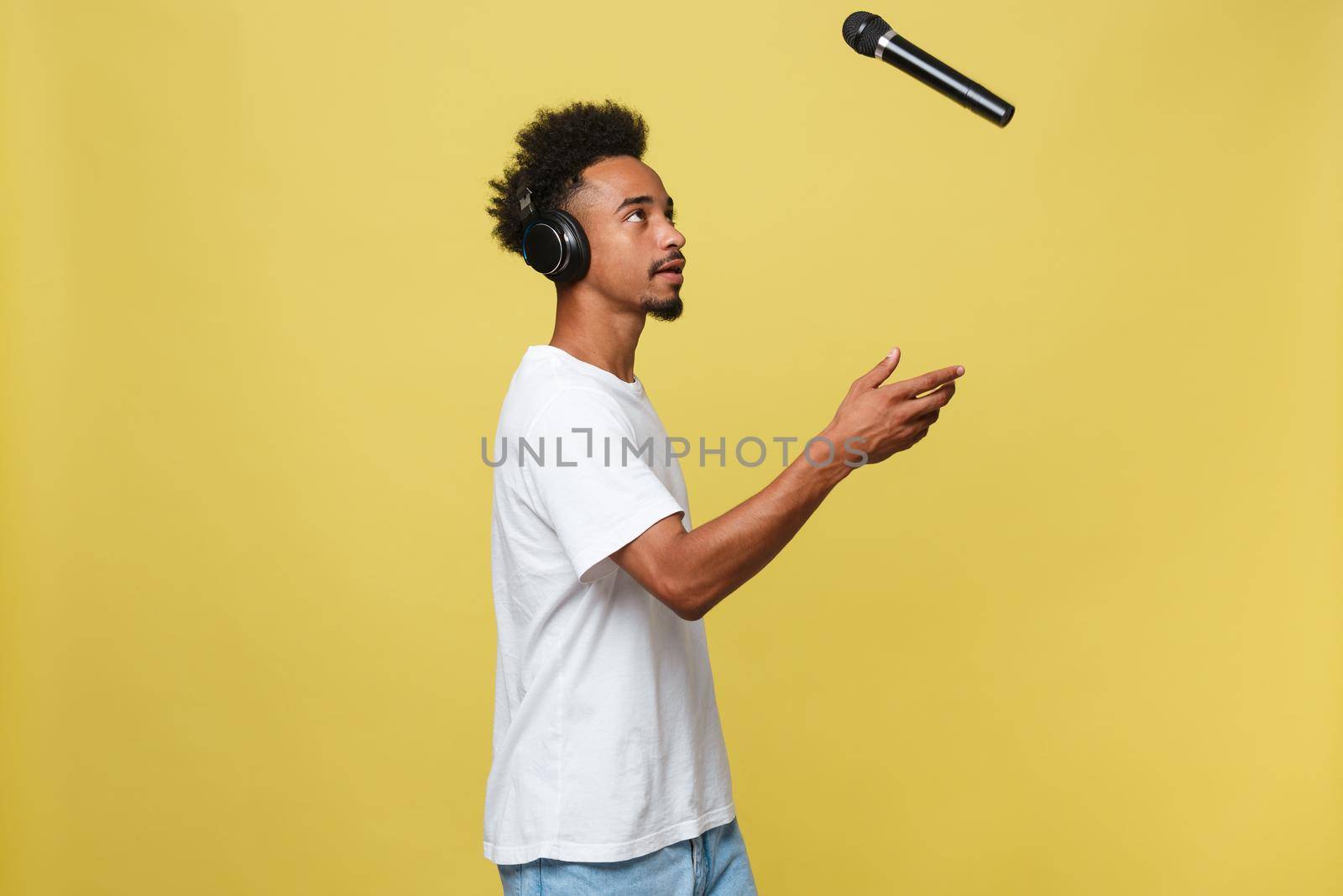 Handsome Black man throwing a microphone and singing. Isolated over a yellow background