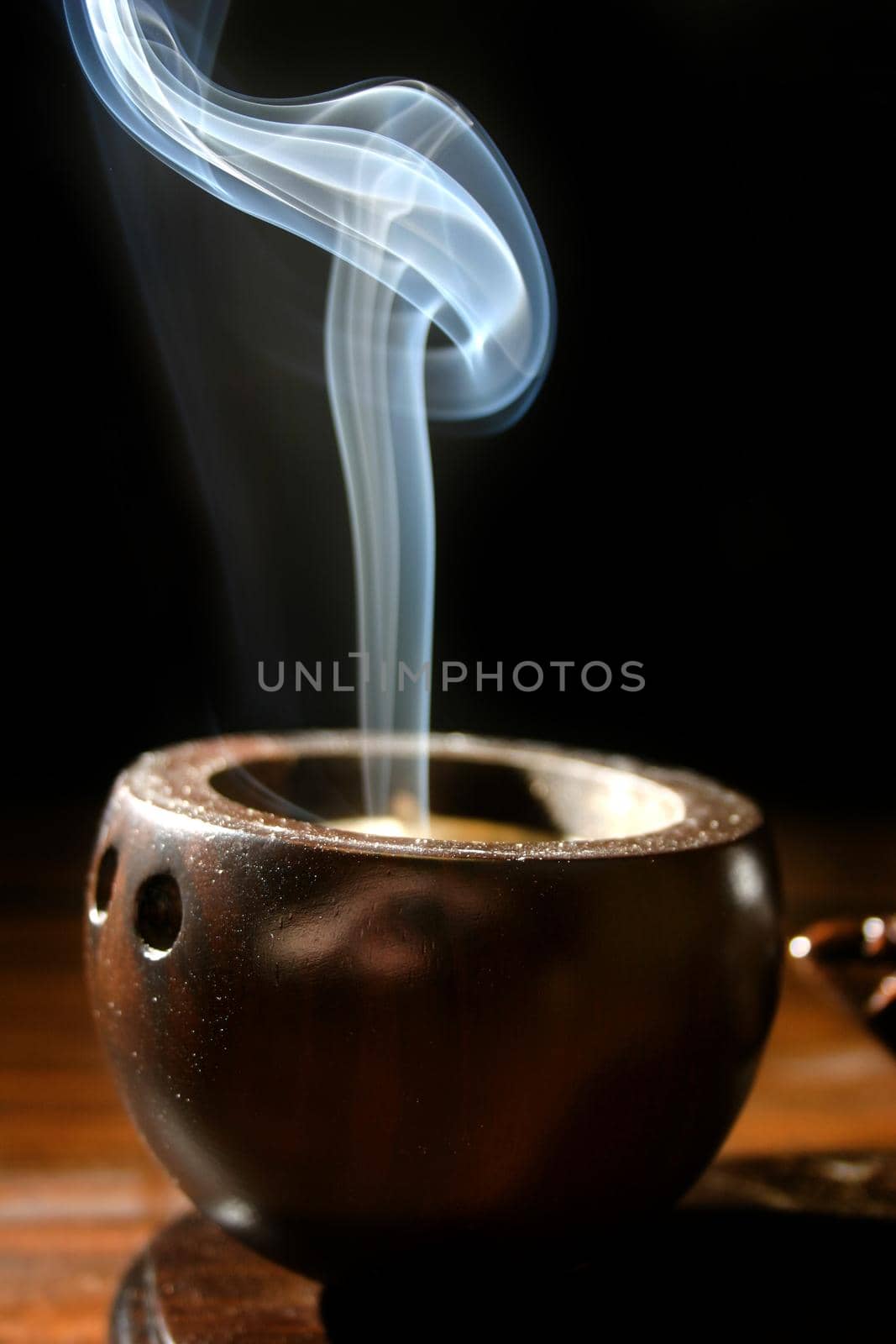 Image of A thin trail of smoke rises from a brown cup-like incense holder