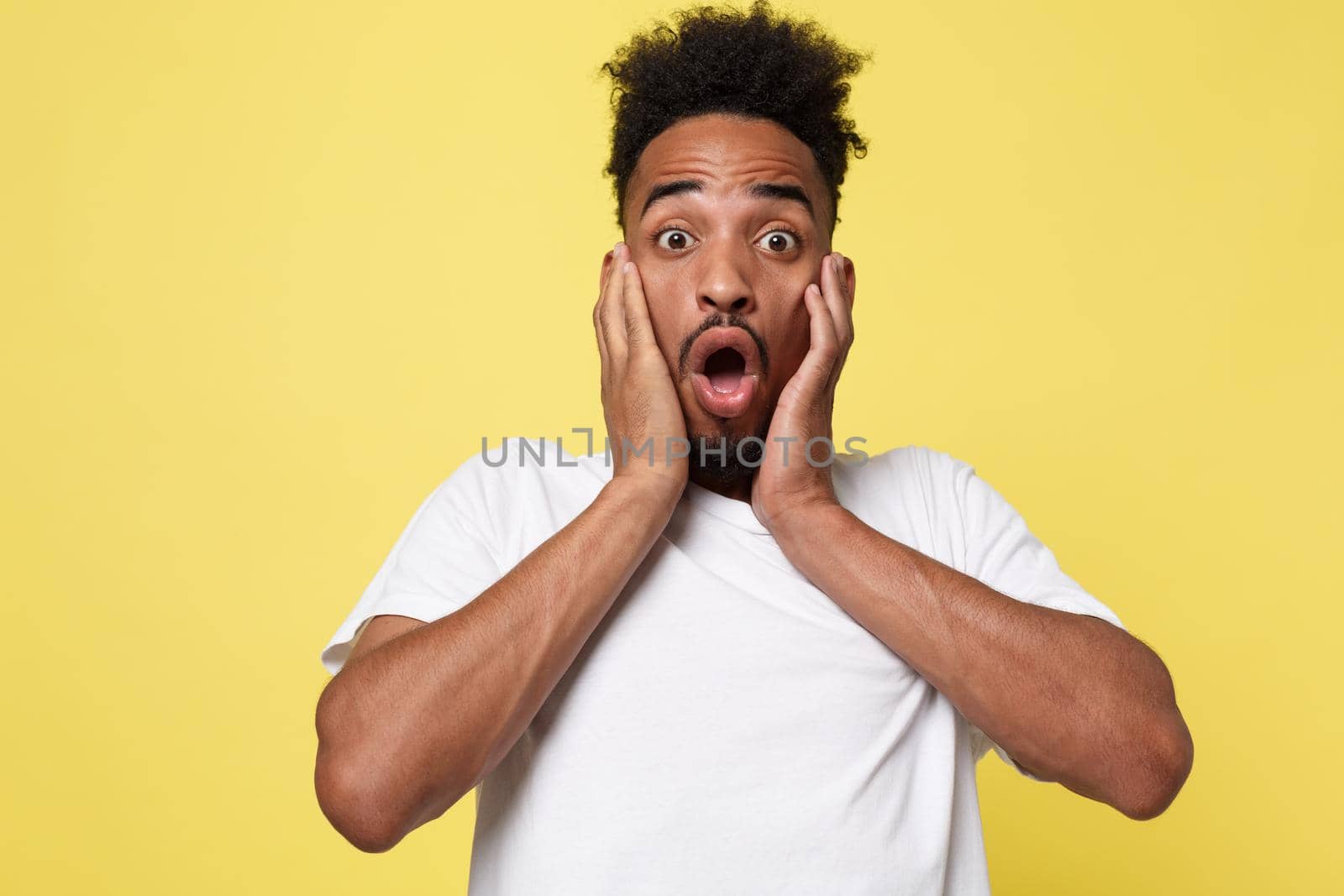 Emotional and People Concept - Portrait of excited young African American man screaming in shock and amazement holding hands on head. by Benzoix
