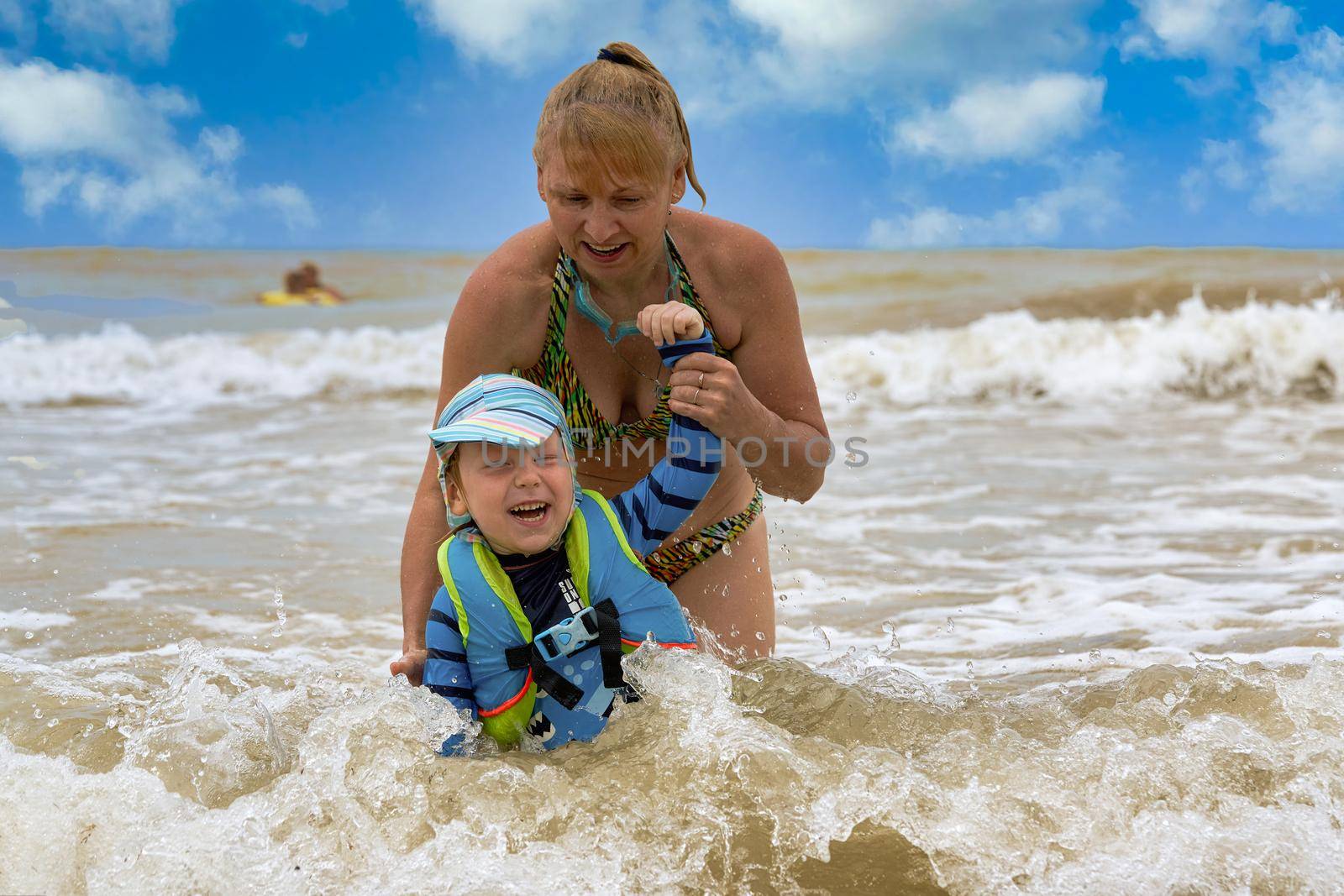 A woman takes a child in a life jacket out of the stormy sea. Vacation safety at sea