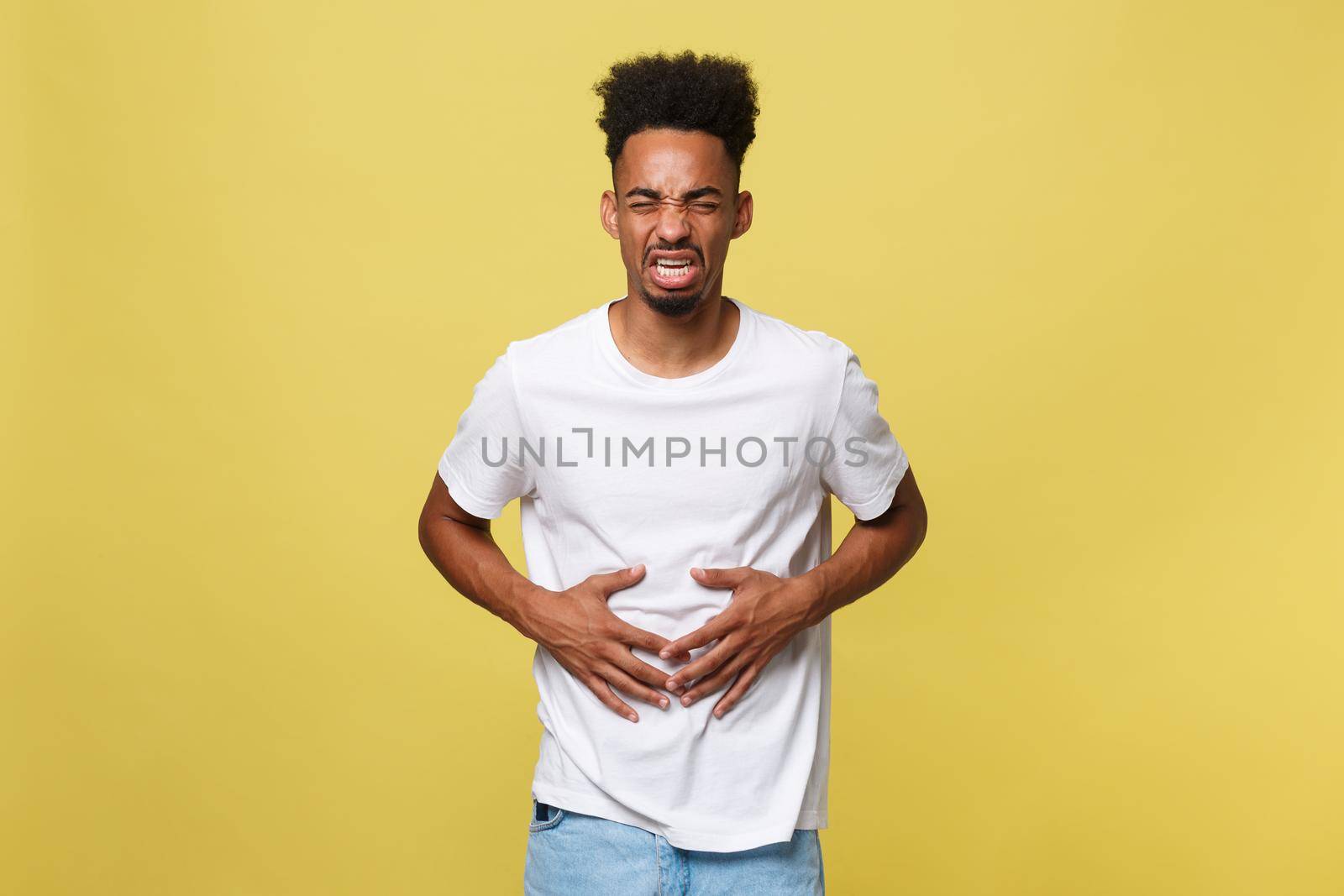 Closeup portrait of miserable, upset, young man, doubling over in stomach pain, looking very sick unwell, isolated on yellow background. Facial expressions emotion feelings, health issues by Benzoix