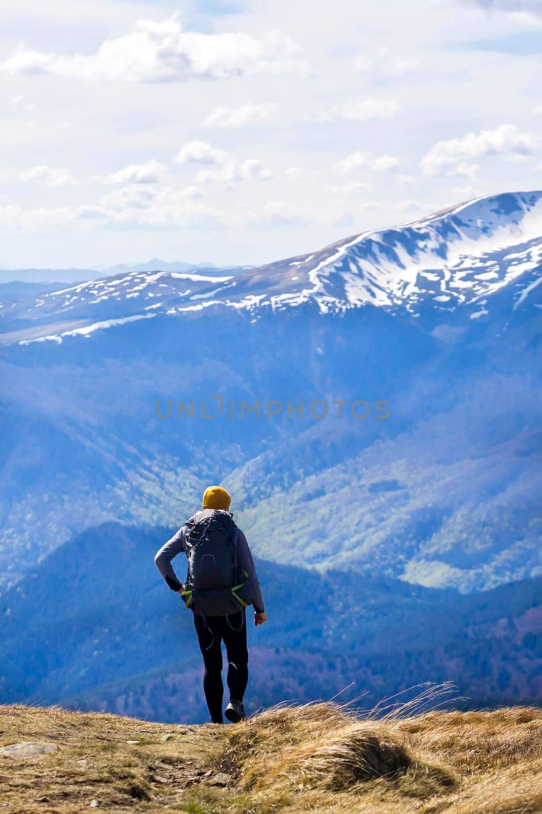 The traveler looks at the stunning view of the snow-capped mountains at sunset. Young man with a backpack and tourist equipment is hiking in the national park in winter, engaged in extreme sports.