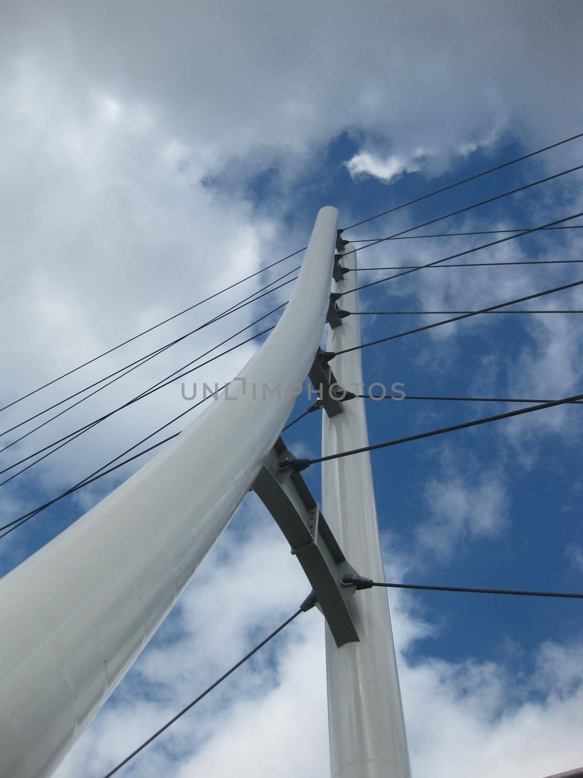 Image of Worm's eye view of a white triangular bridge with suspension cables crisscrossing a blue and cloudy sky