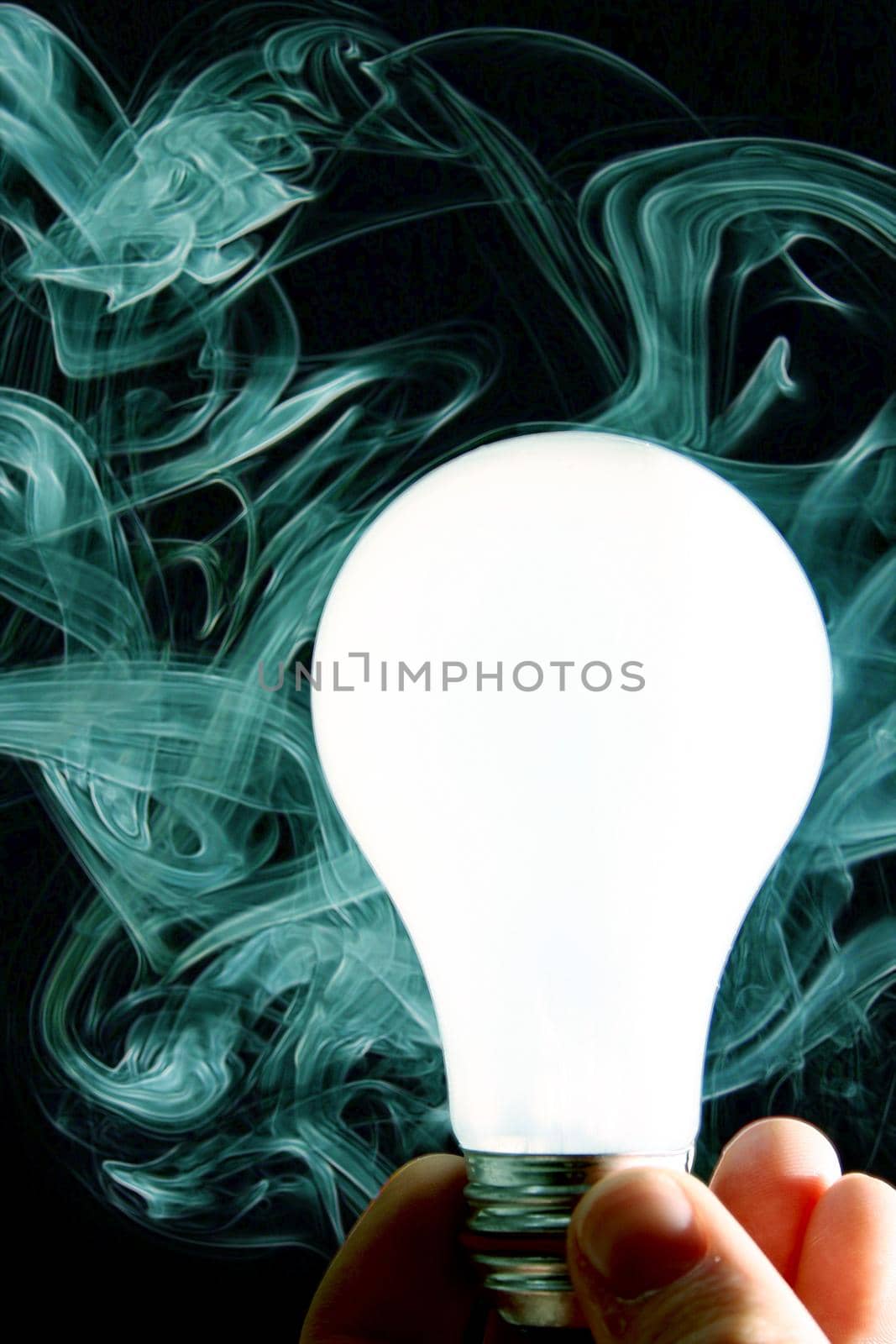 Image of White lightbulb held by a human hand against a background of teal smoke and black