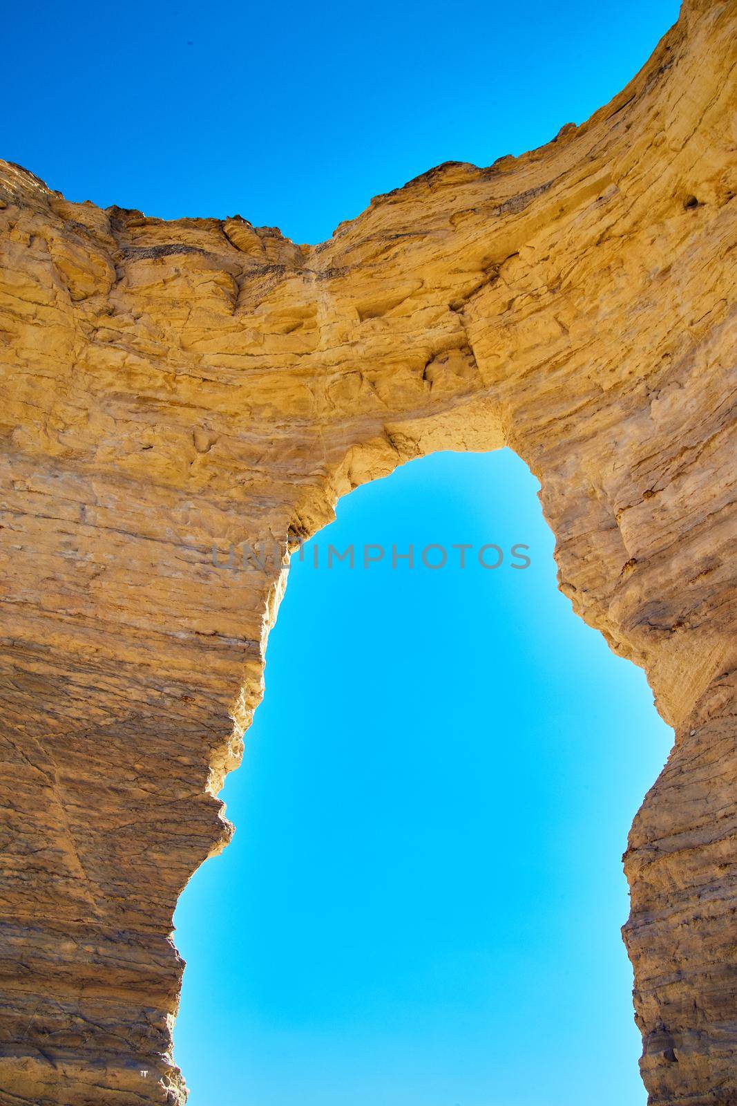 Image of Vertical open natural arch cutting through white stone against blue sky