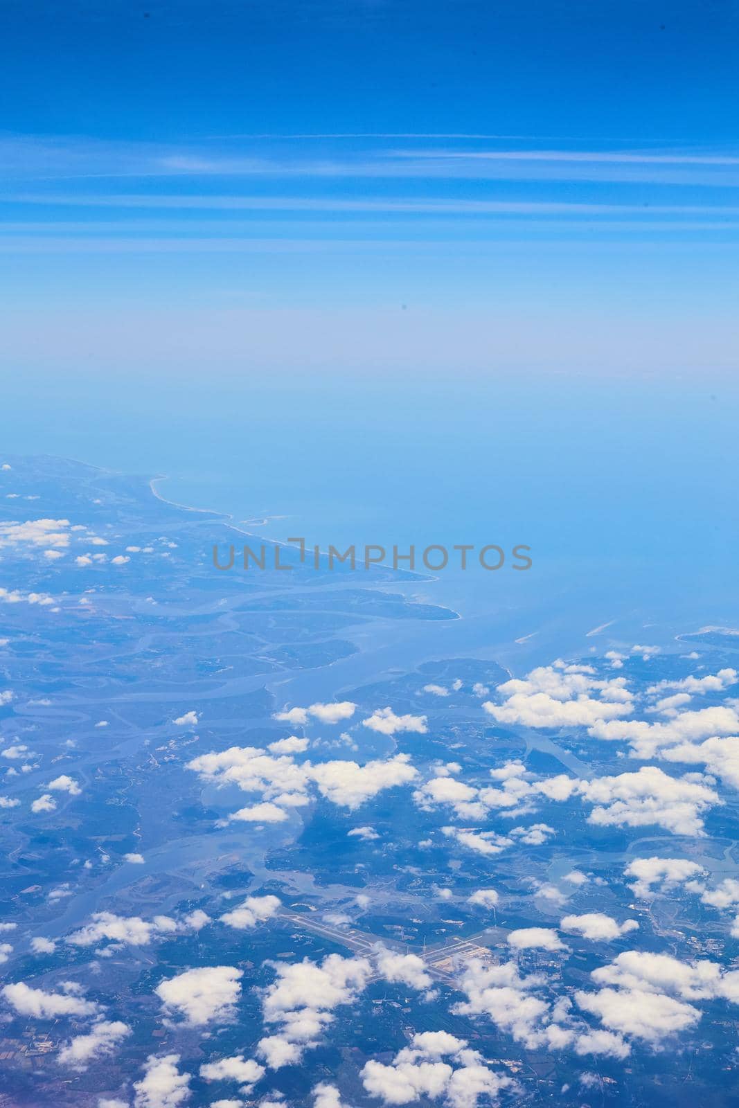 Image of Airplane view of clouds and blue sky with land in distance