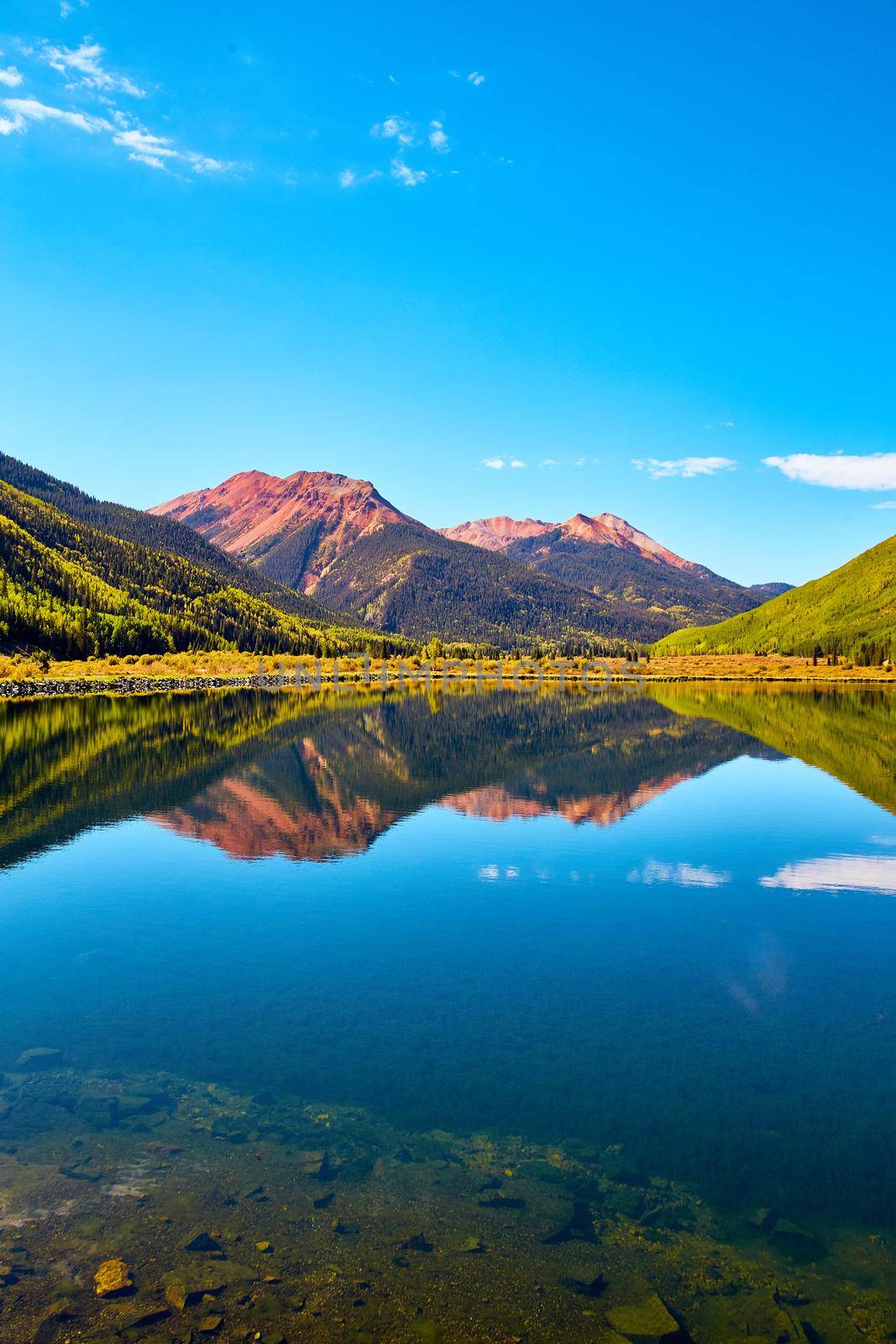 Image of Vertical landscape of lake in the mountains with fall aspen trees and red sandy mountain peaks against blue sky