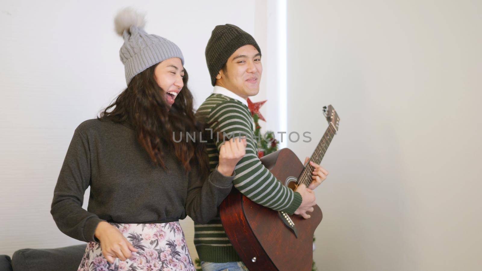 Happy Asian beautiful young family couple husband and wife on in home living room, man and woman playing the guitar, singing song and dancing together enjoying great time in living room,
