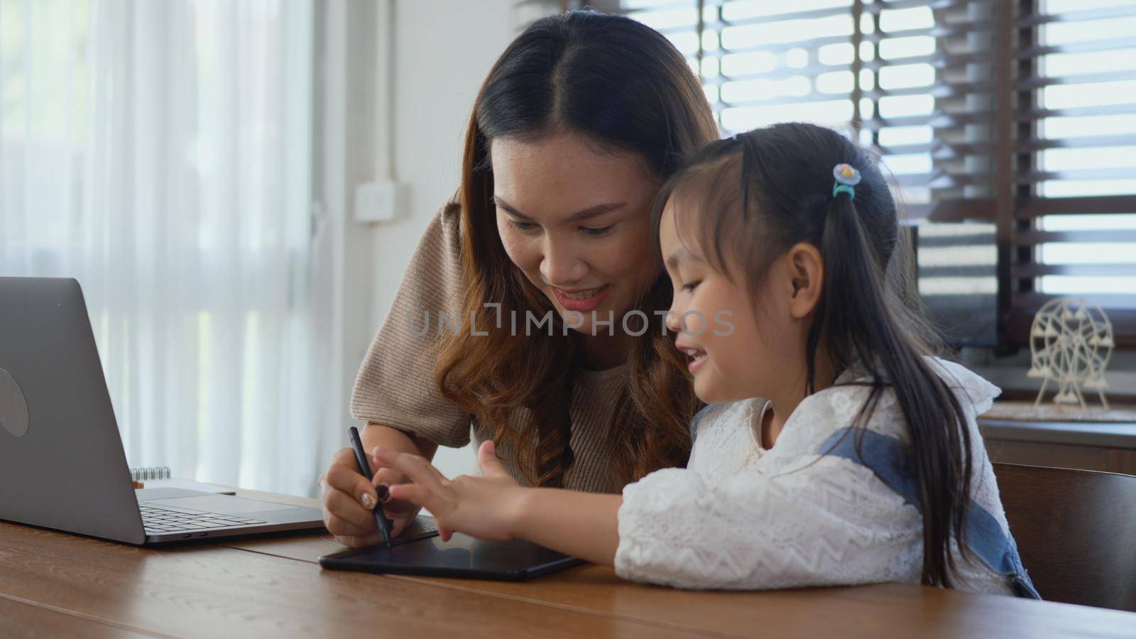 mother working with laptop computer at home and help daughter doing homework by Sorapop