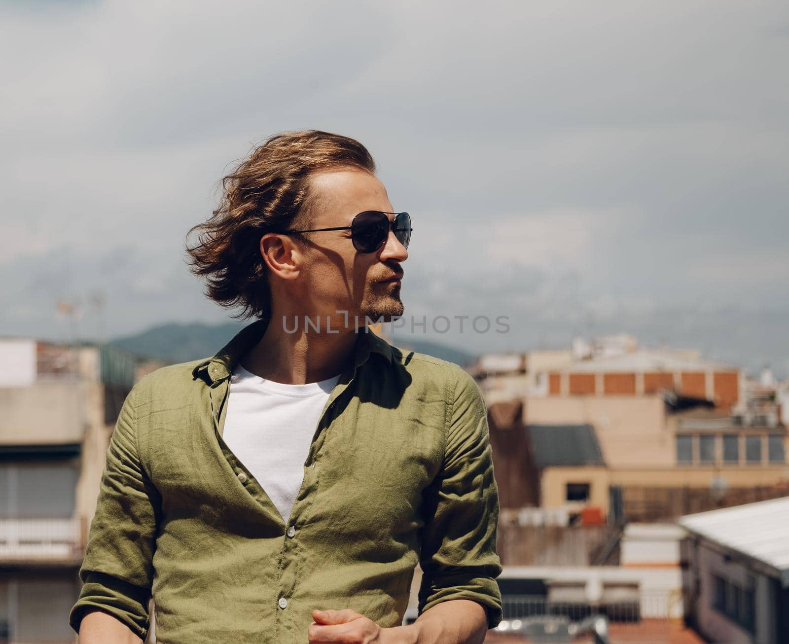 Handsome european man in sunglasses with long hair, standing outdoors and looking to the side