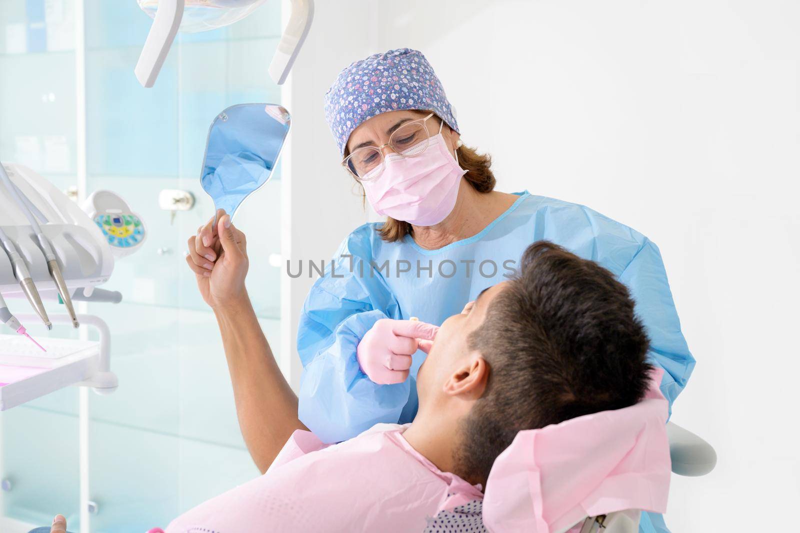 Patient looking teeth in mirror at dental clinic by HERRAEZ