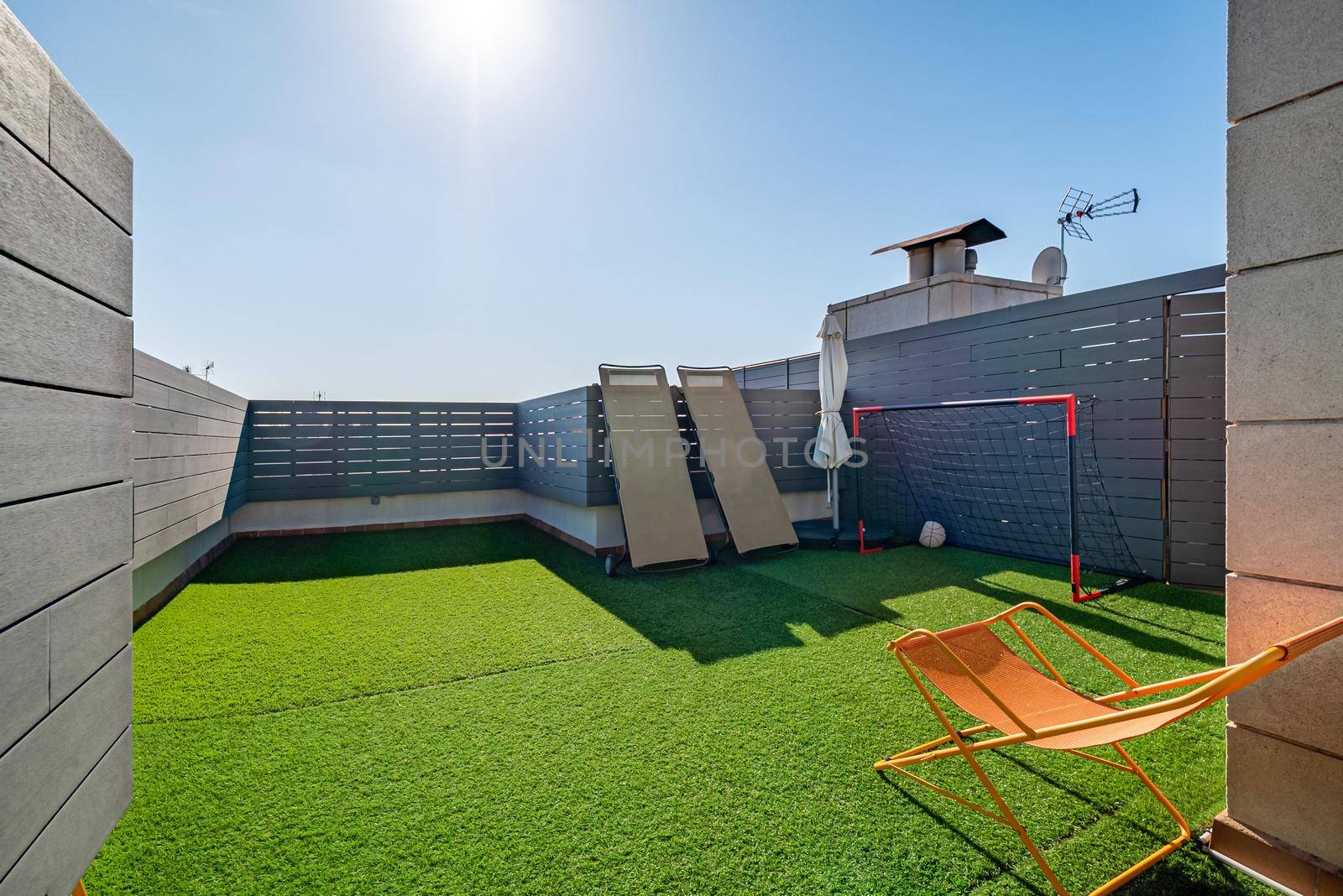 Private terrace with sunbeds, kids soccer gates and artificial turf on sunny day with blue sky