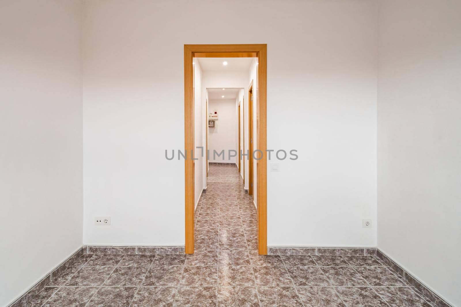 Empty room in apartment with long corridor, tiled floor and white walls.