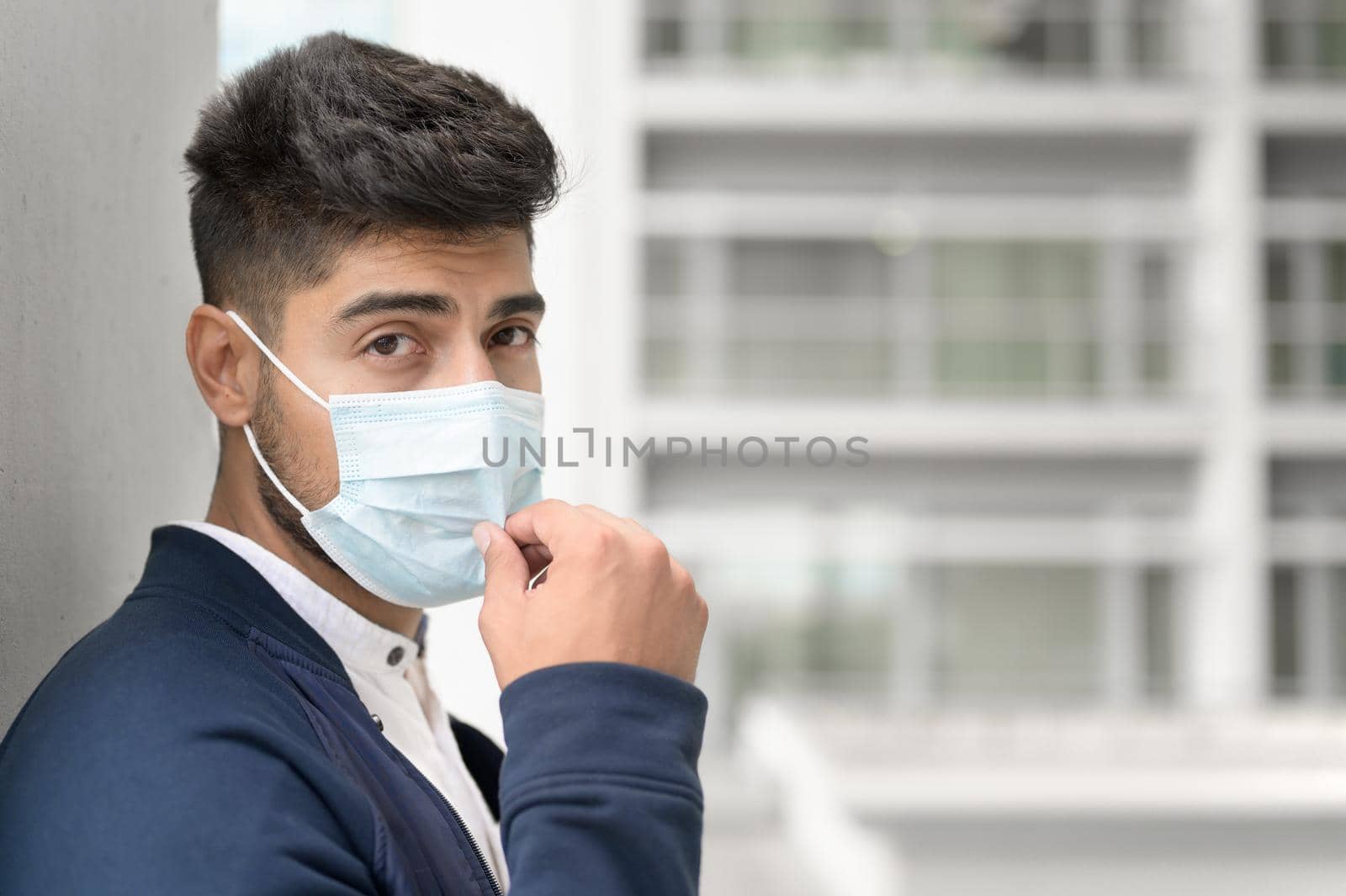 Portrait of a Handsome man in medical mask looking to camera at city. Handsome young man standing outdoors in medical mask. Coronavirus concept. by HERRAEZ