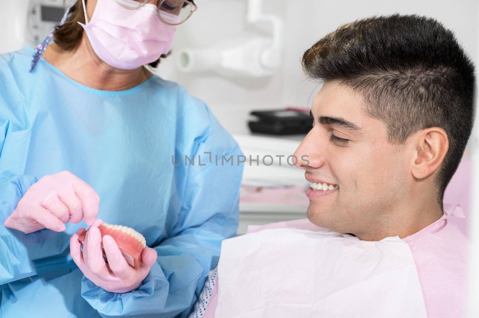 Orthodontist holding invisible retainer for teeth alignment. In clinic shows patient modern dental technology - removable transparent plastic aligners or invisalign use and benefit. by HERRAEZ