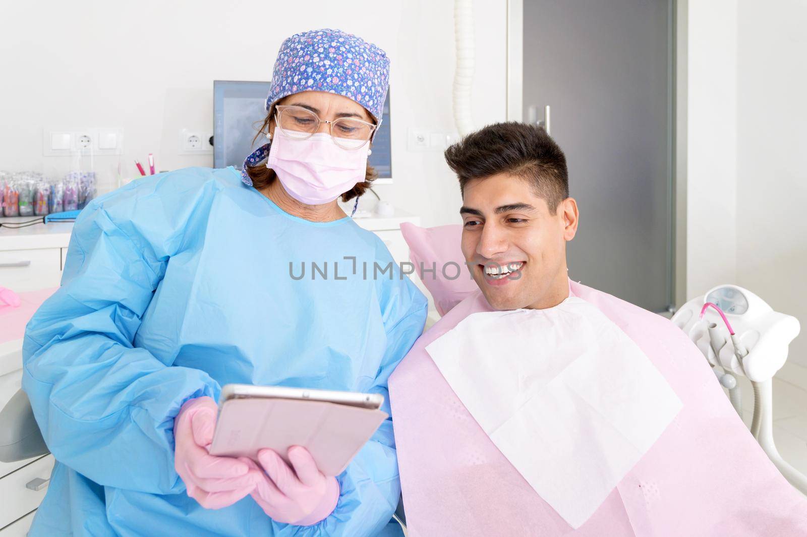 Dentist and patient commenting treatments in a tablet application in a consultation with medical equipment in the background. High quality photo.