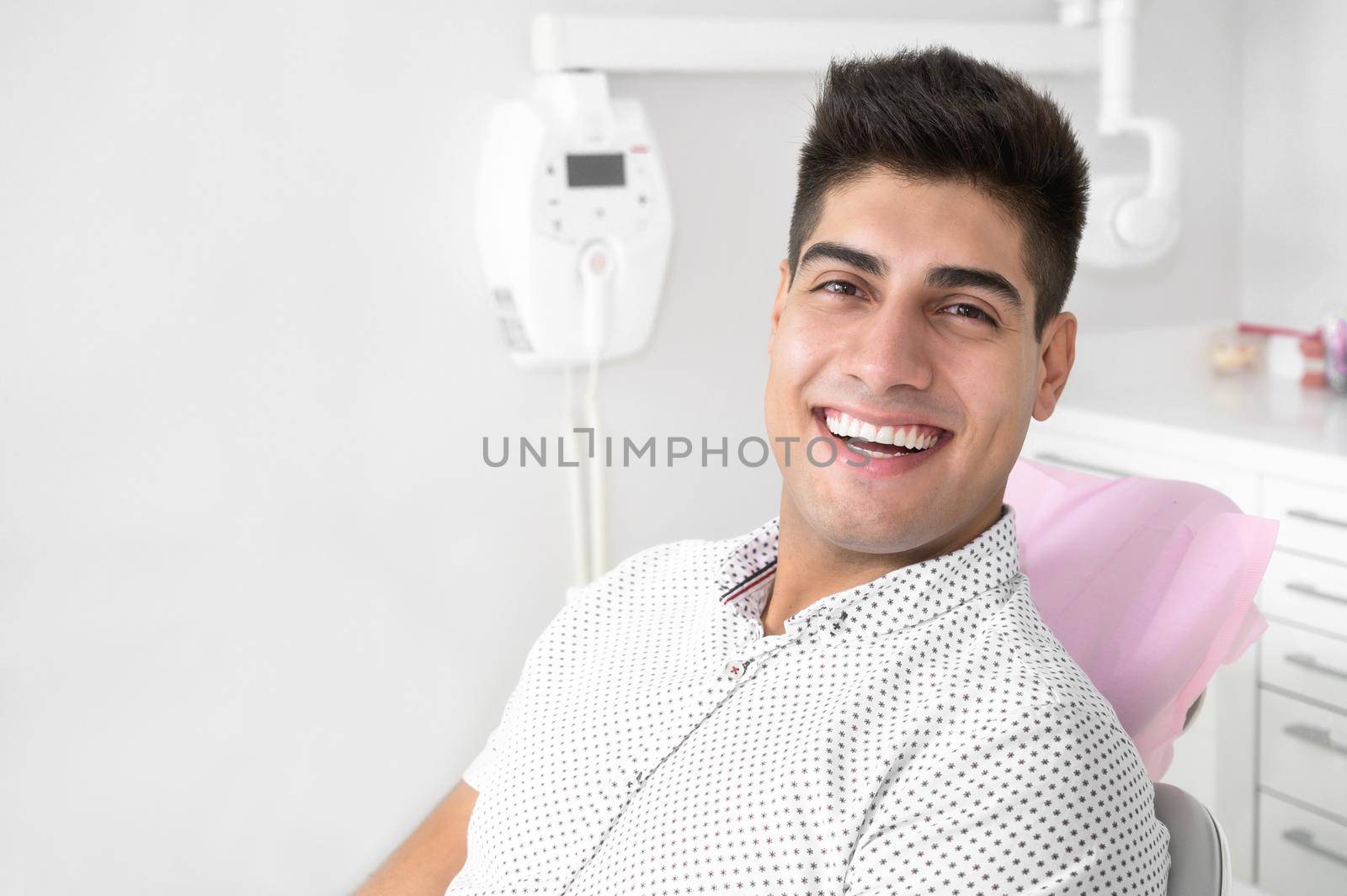 Portrait of a positive handsome patient smiling looking at camera, after treatment at dental clinic. by HERRAEZ
