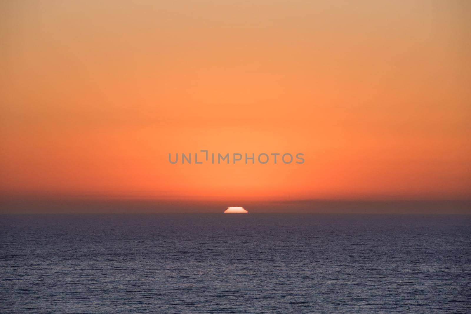 Sunset over the ocean horizon with bright orange sky by jyurinko