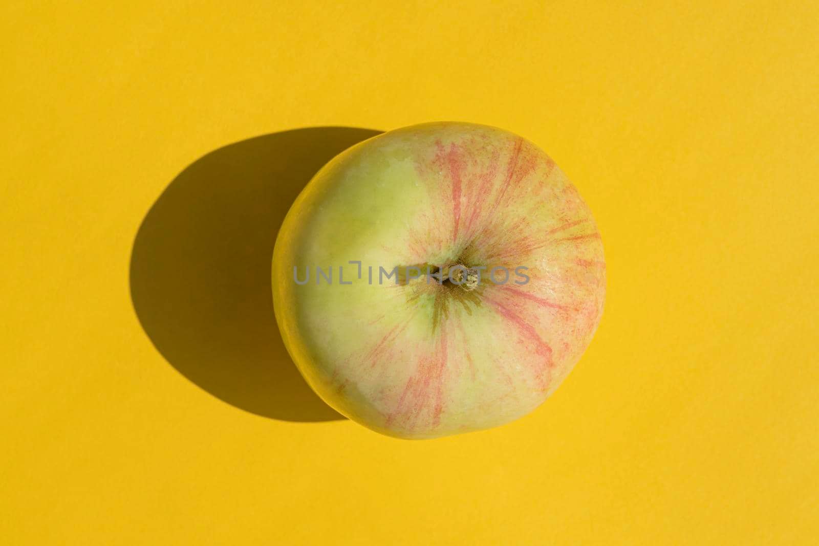 an apple with a hard shadow on a yellow background by roman112007