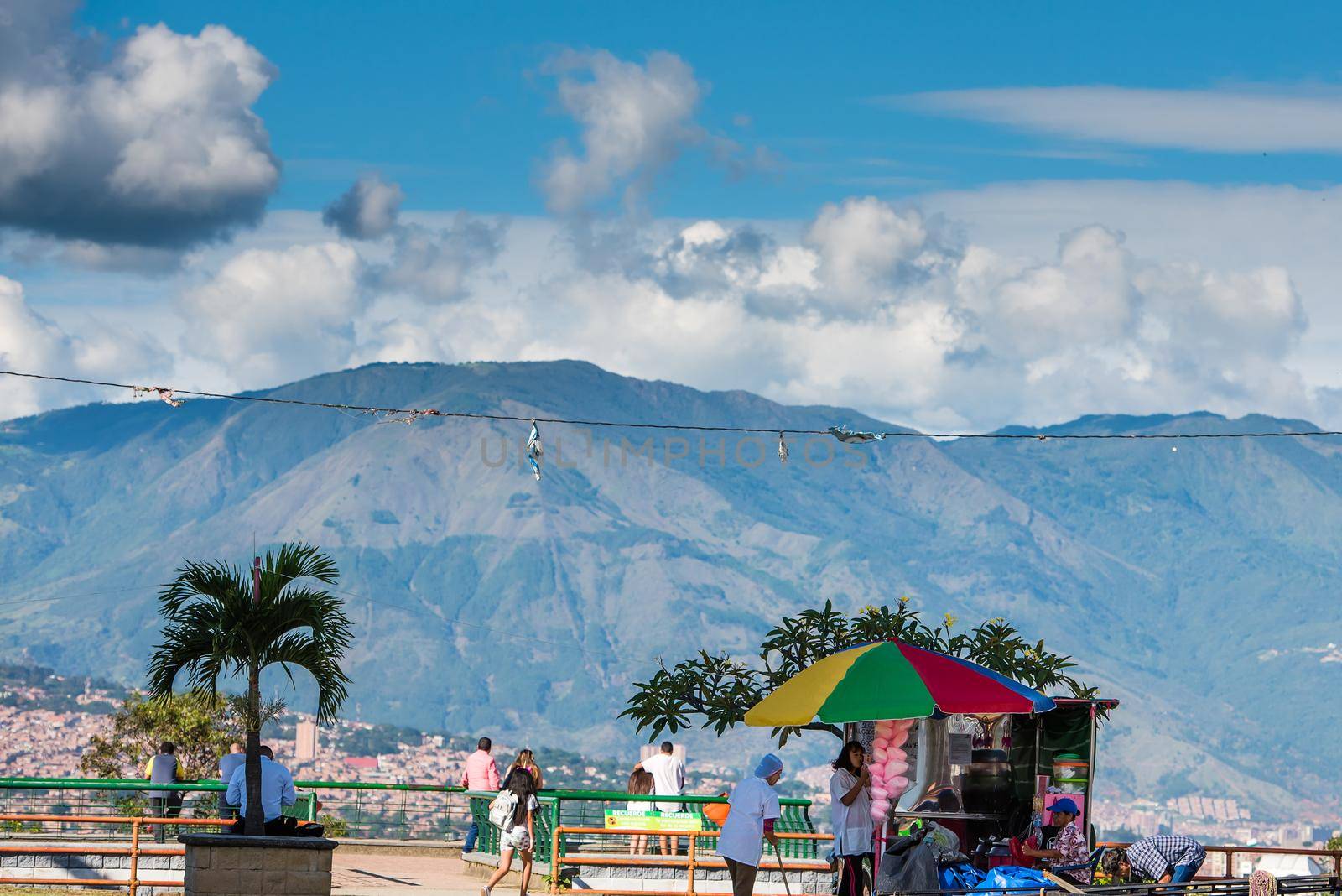 Palm tree and colorful umbrella and puffy clouds over mountains in Bogota Colombia. by jyurinko