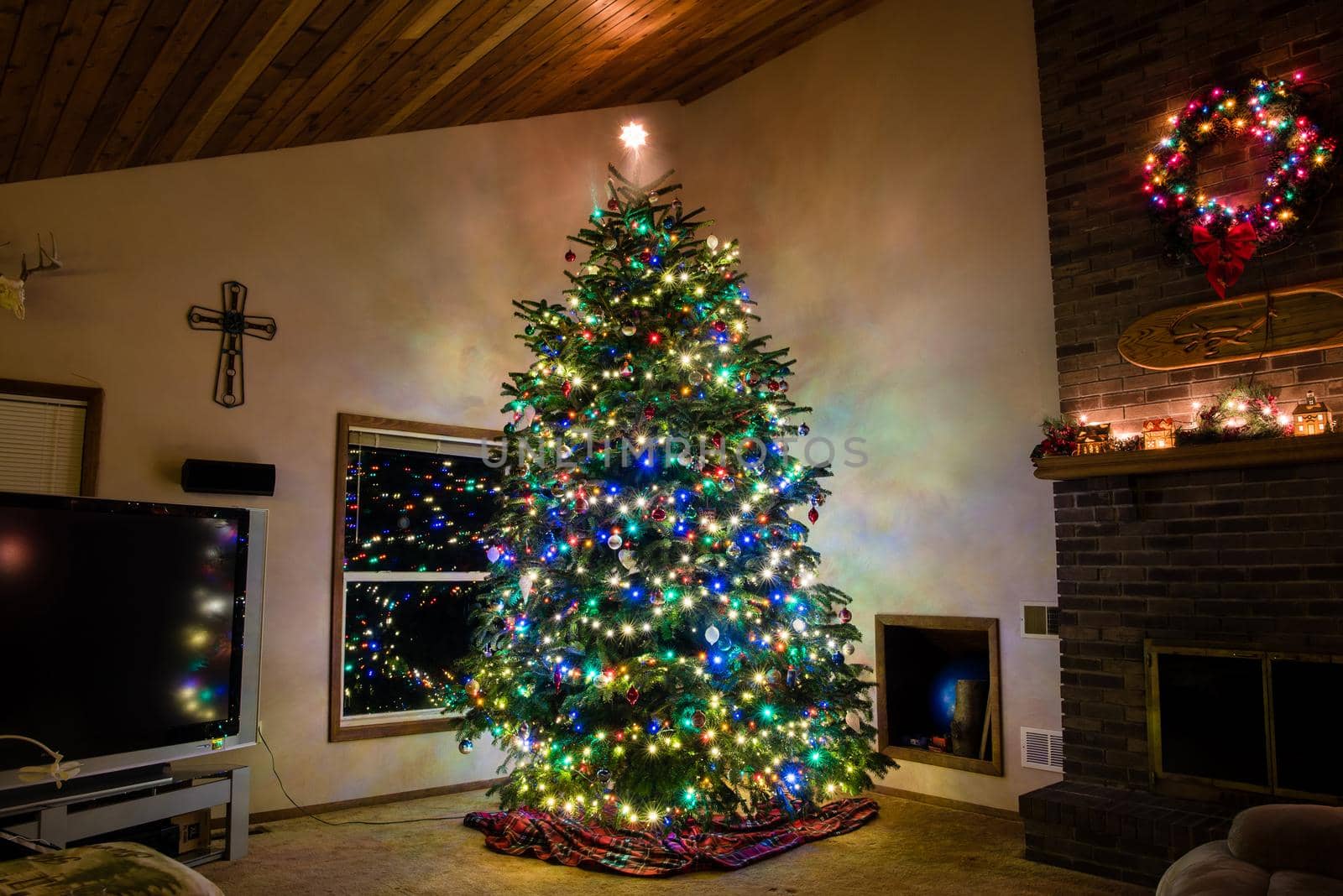 Large Christmas tree lit up in living room with wreath and cross. by jyurinko