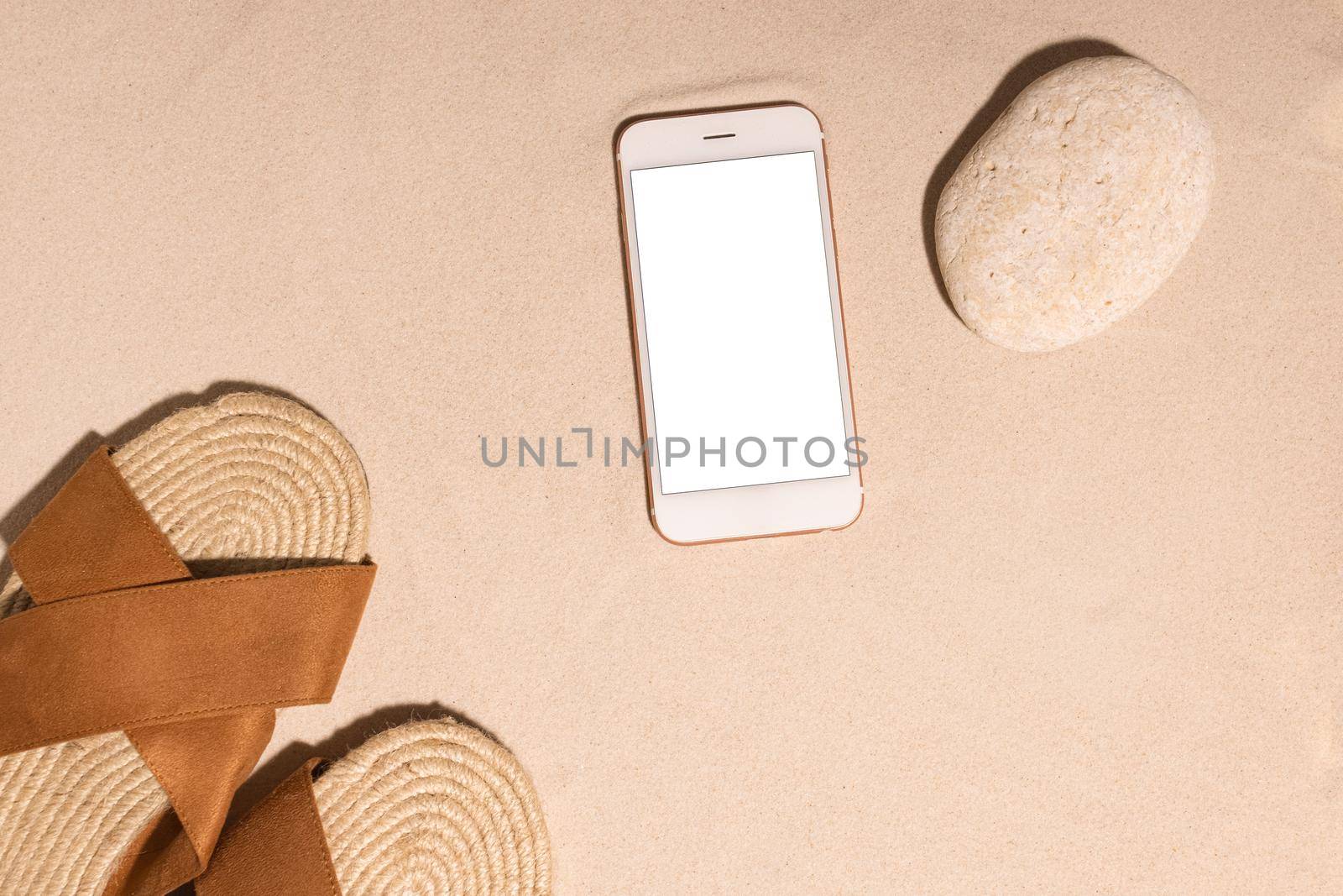 Beach background with mobile phone ,brown sandals and stone on a sandy beach in the sun. Concept: Summer vacation in a warm country. by katrinaera