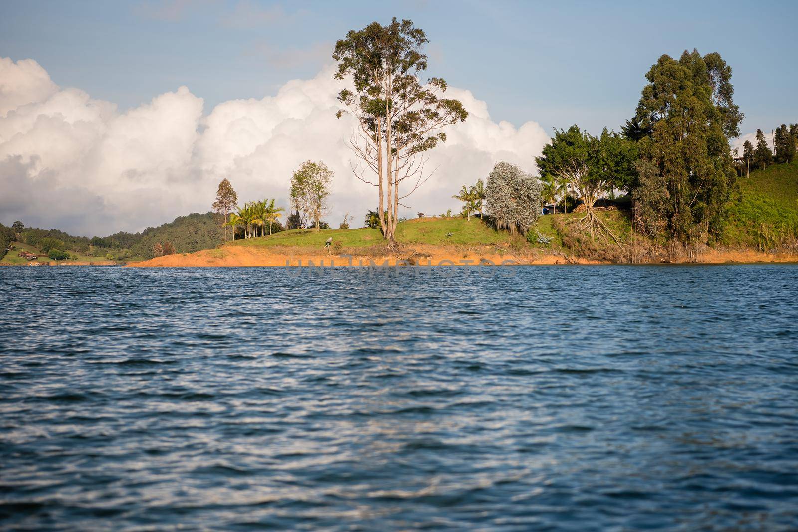 Lush landscape with cloudy blue sky in the background and water in the foreground. View from a boat