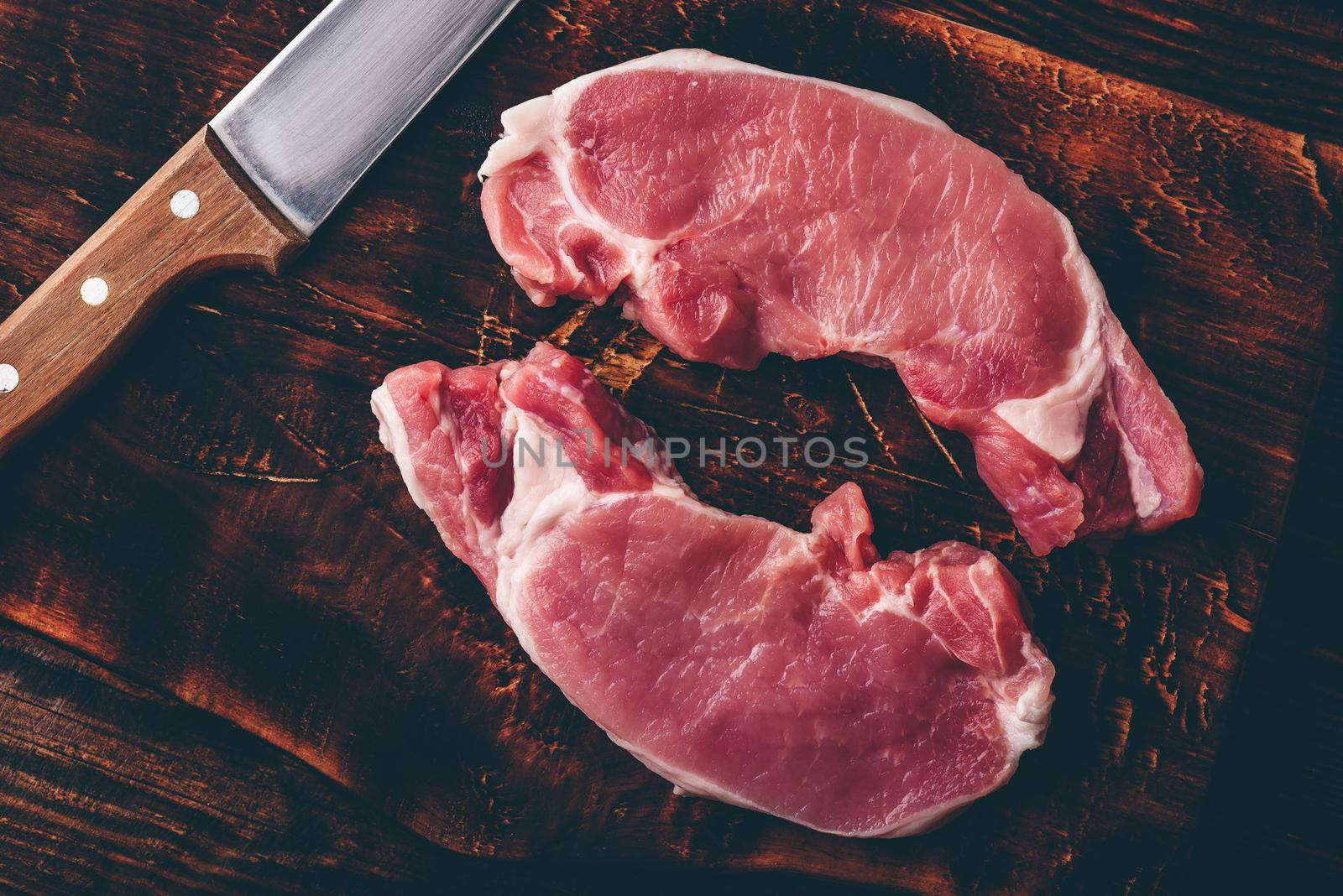 Two pork loin steaks with knife on rustic cutting board
