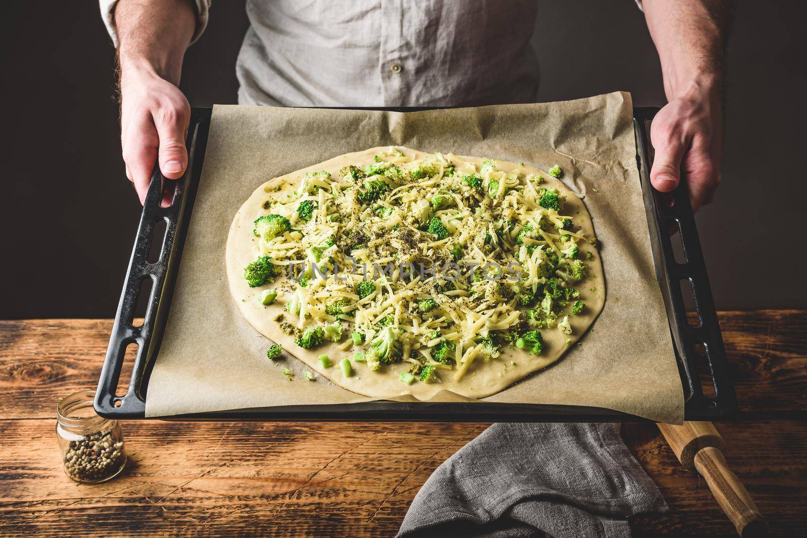 Man holding uncooked pizza with broccoli and cheese by Seva_blsv
