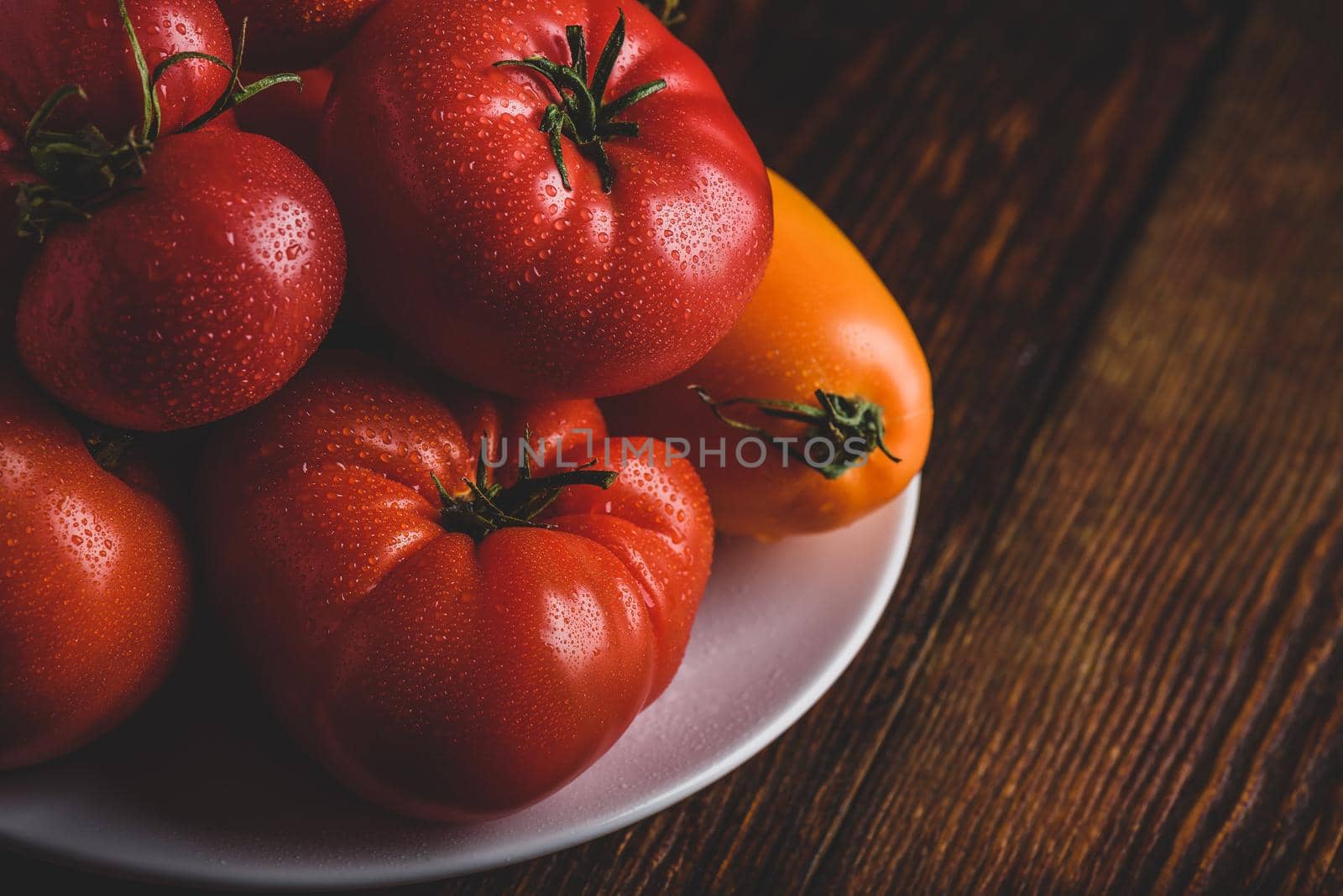 Fresh red and yellow tomatoes on white plate over wooden surface