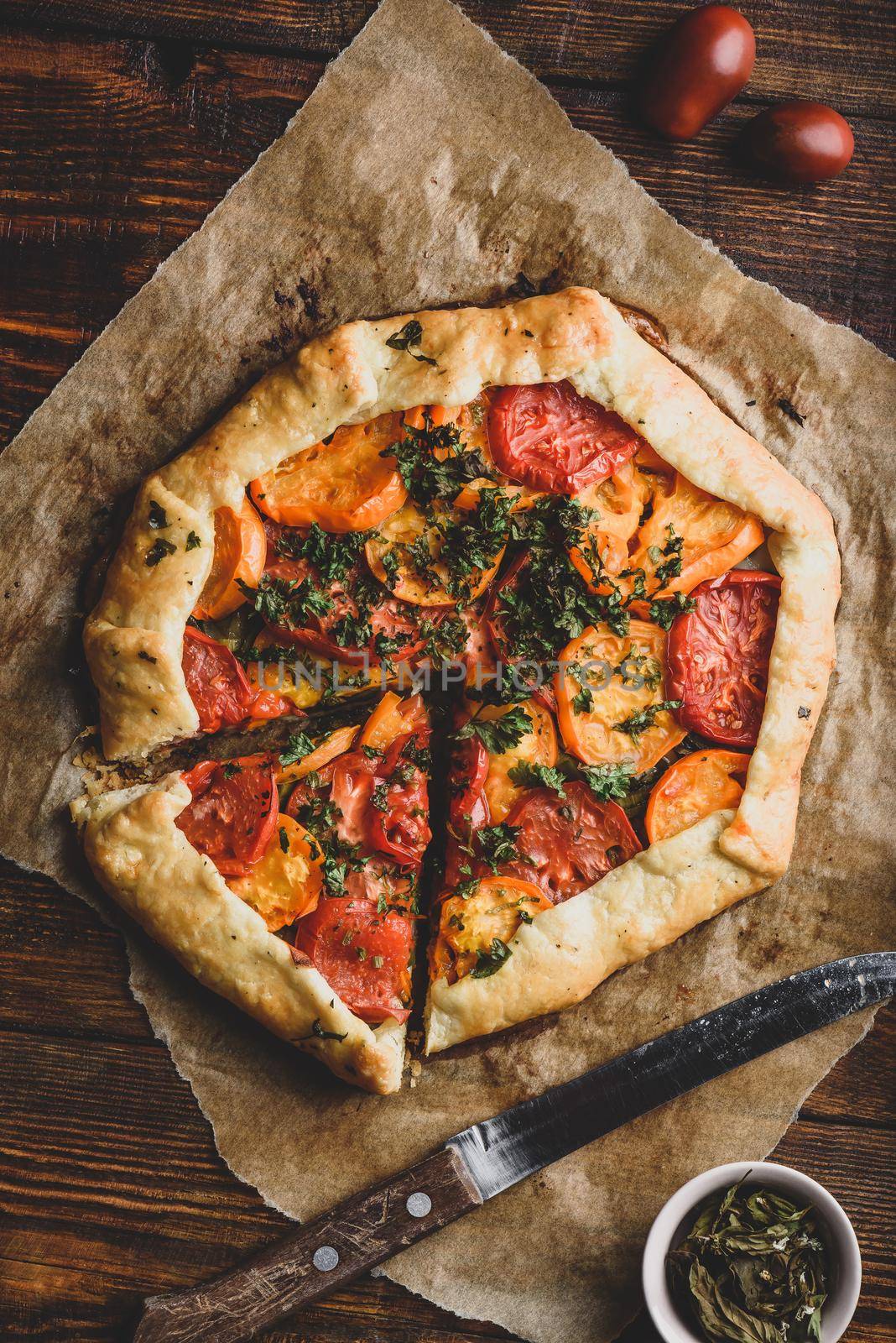 Freshly baked and sliced tomato galette on baking paper. View from above