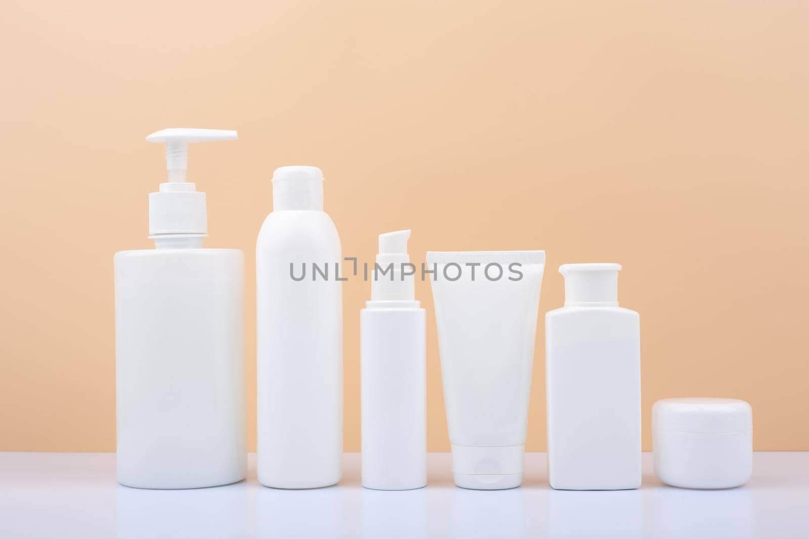 Set of white unbranded cosmetic bottles for face and body care in a row against bright beige background. Concept of organic, natural, eco friendly cosmetics and beauty products