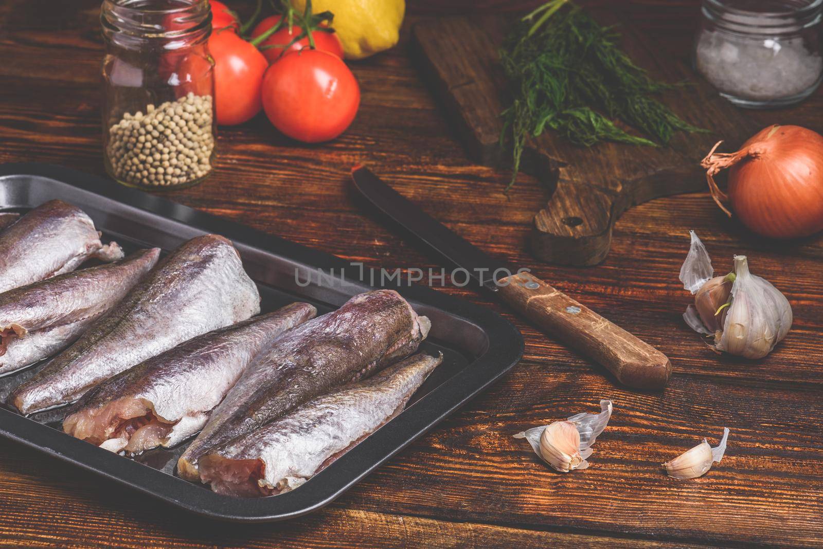 Hake carcasses on baking sheet with vegetables and spices